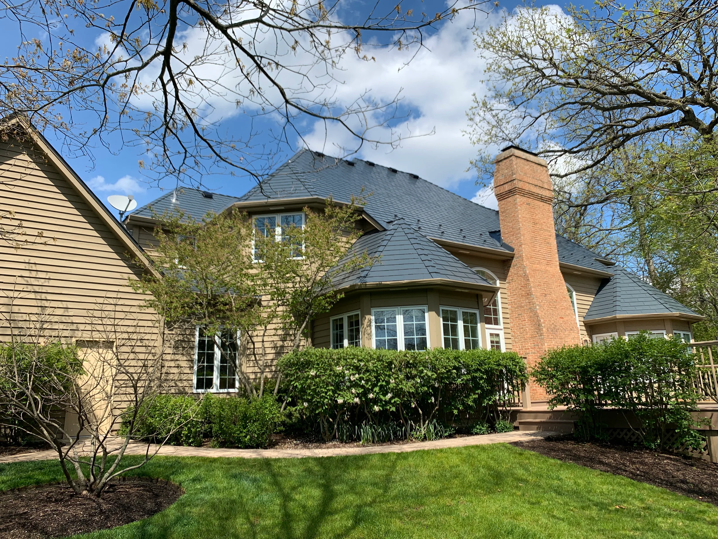 Deep Charcoal Interlock Slate aluminum roof on a tan two-storey Colonial home with dormers among tall pines, Crystal Lake, Illinois