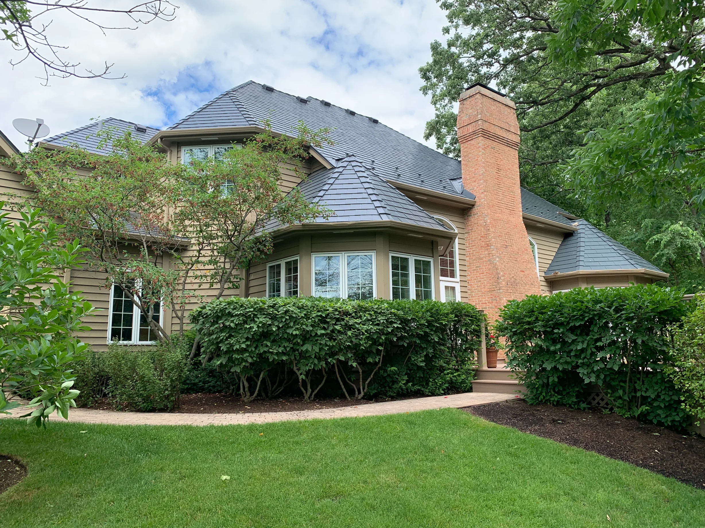 Deep Charcoal Interlock Slate aluminum roof on a tan two-storey home with dormers among tall trees and a, Crystal Lake, Illinois