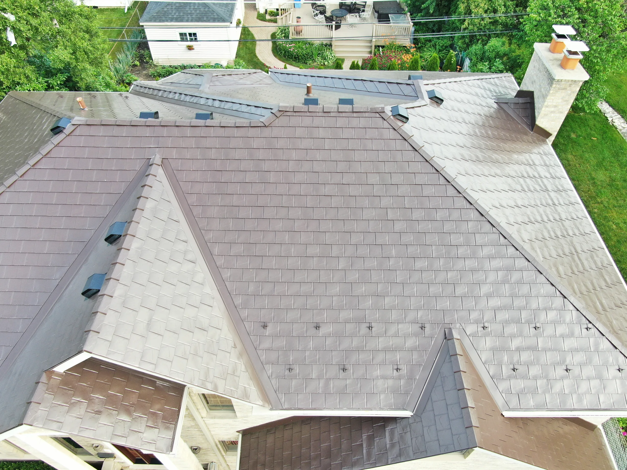 Colonial Brown Interlock Slate aluminum roof on a colonial-style home among tall trees in a suburban area, Calredon Hills, Illinois