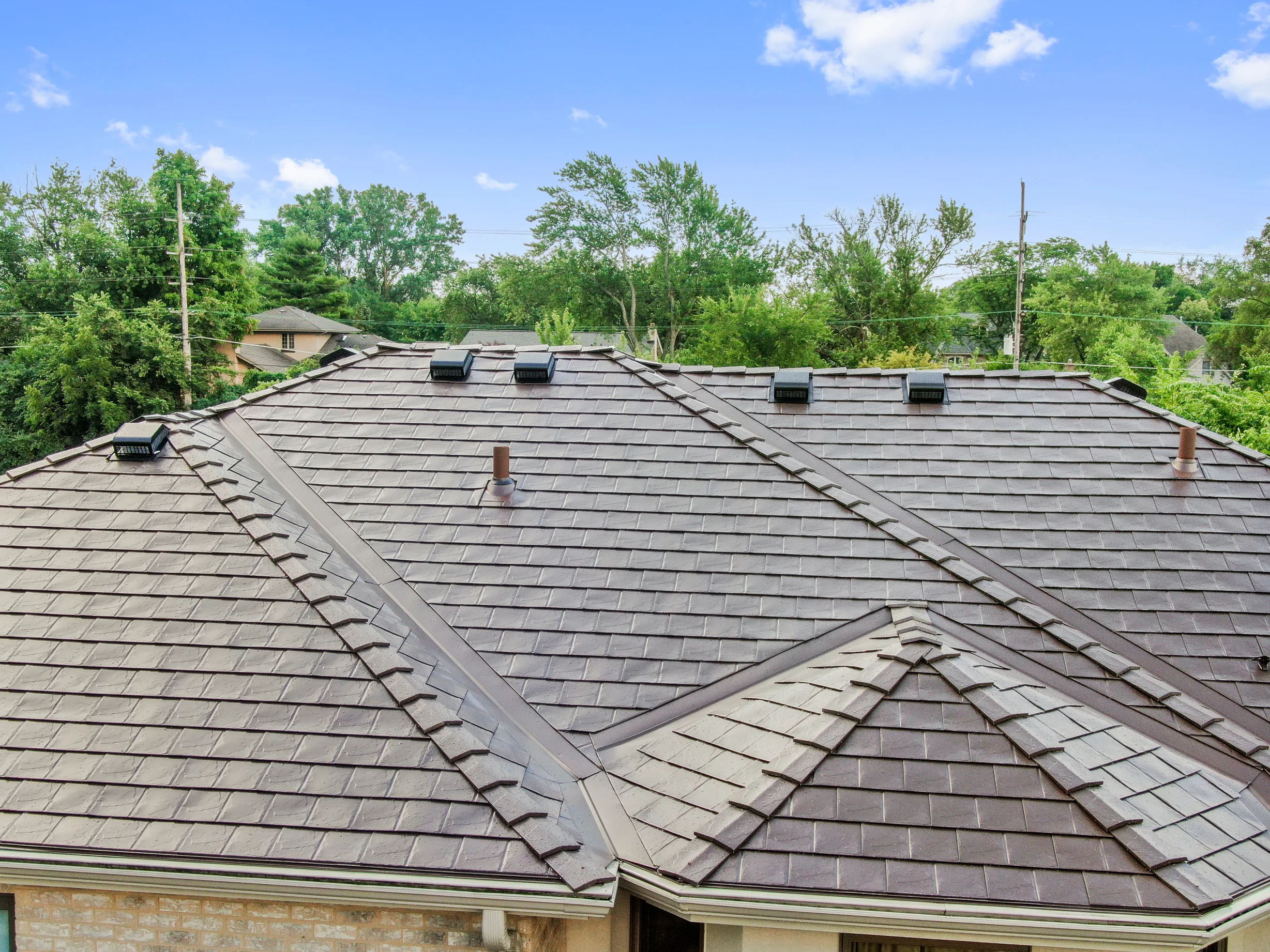 Colonial Brown Interlock Slate aluminum roof on a brown Colonial home with dormers among tall green trees, Calredon Hills, Illinois