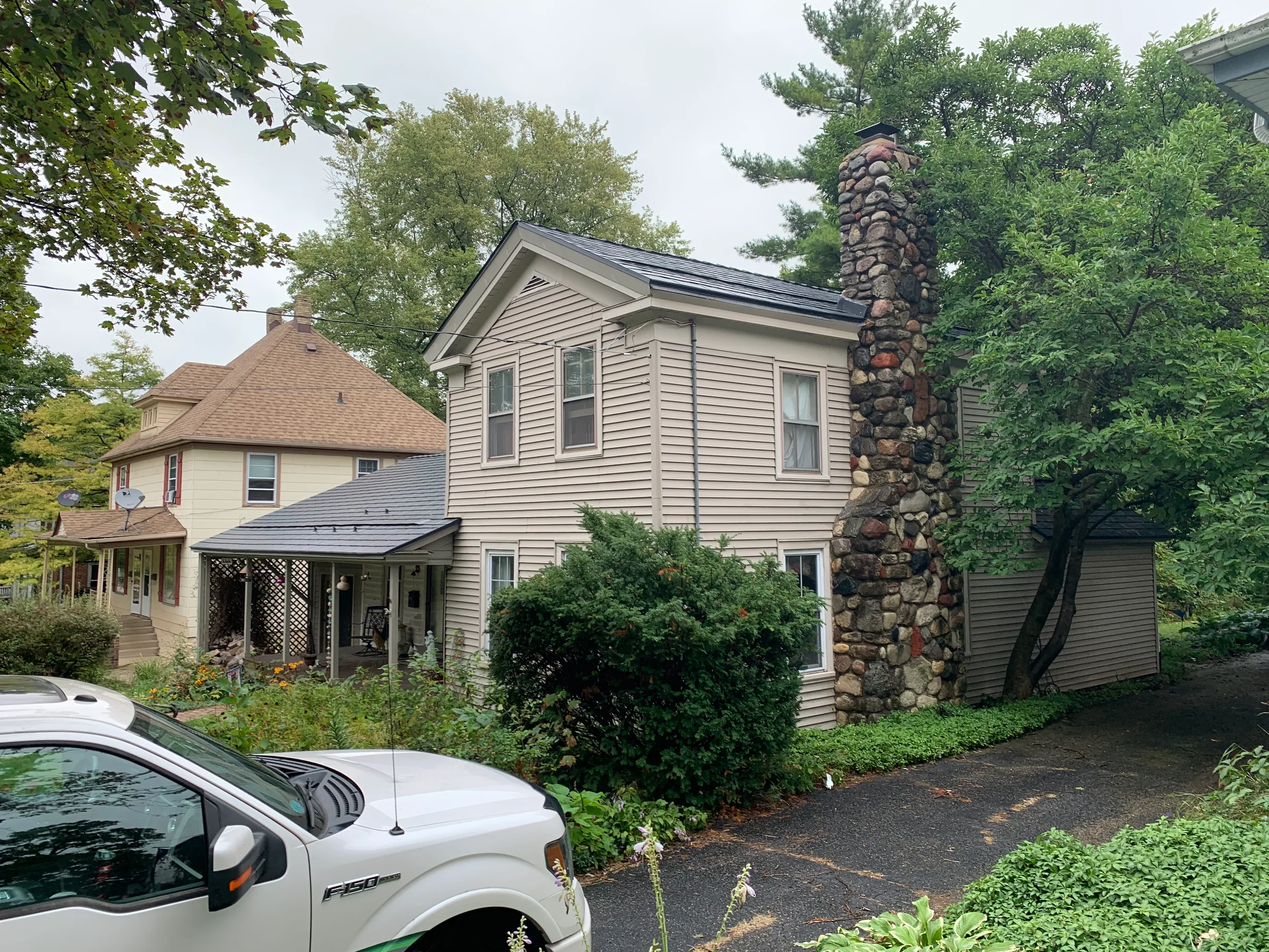 Black Interlock Slate aluminum roof on a beige two-storey colonial home among trees in a suburban, Woodstock, Illinois