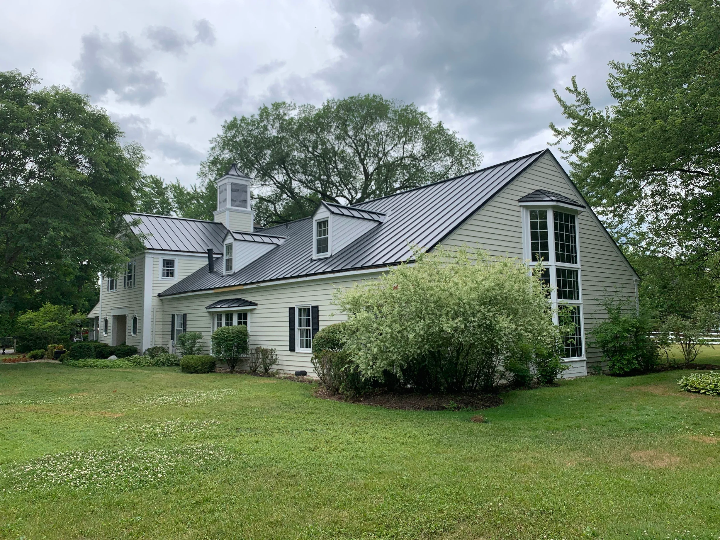 Black Interlock Standing Seam aluminum roof on a light green home with dormers among tall trees, Lake Forest, Illinois