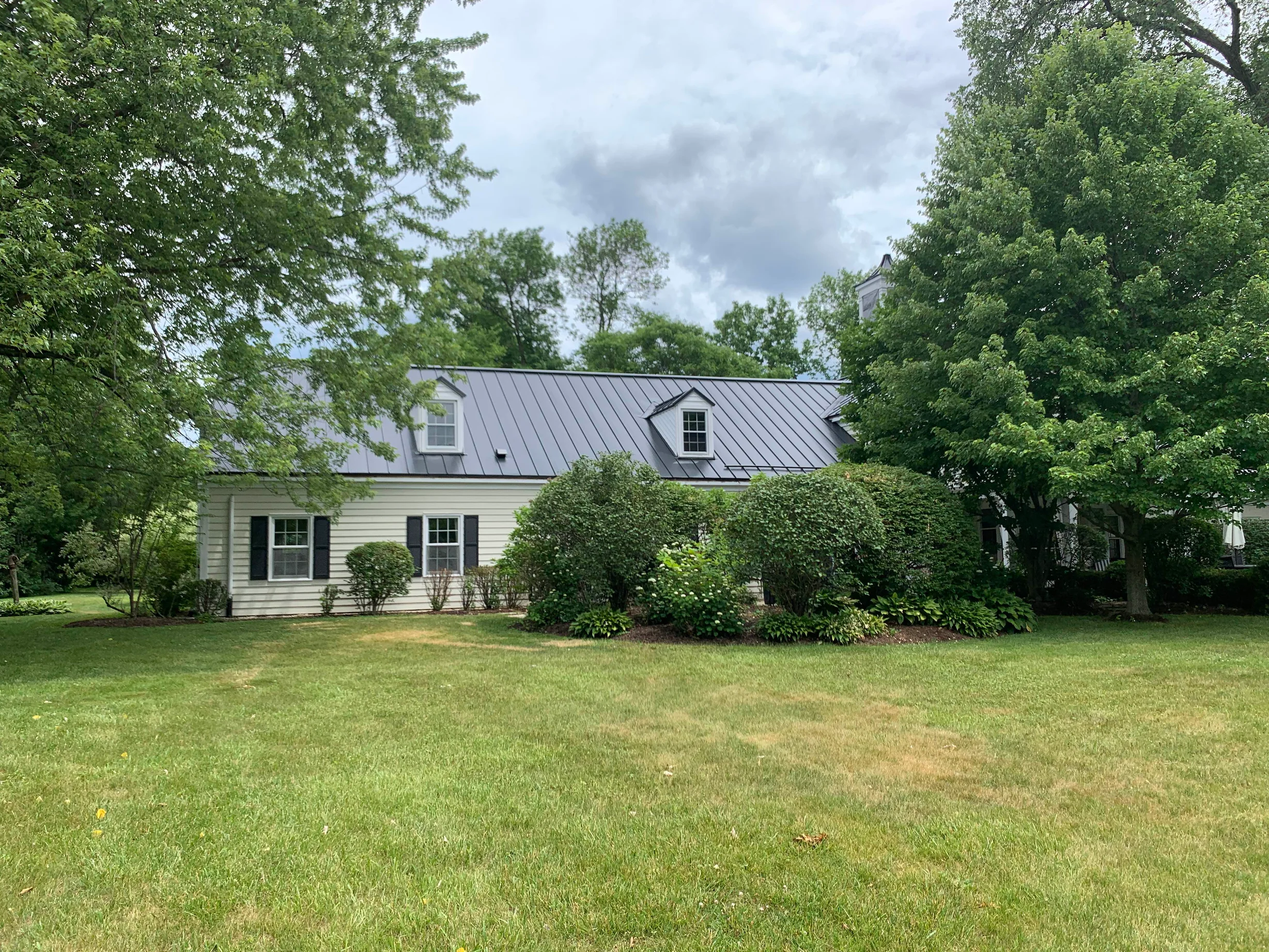 Black Interlock Standing Seam aluminum roof on a white single-family home with a metal roof among tall, Lake Forest, Illinois