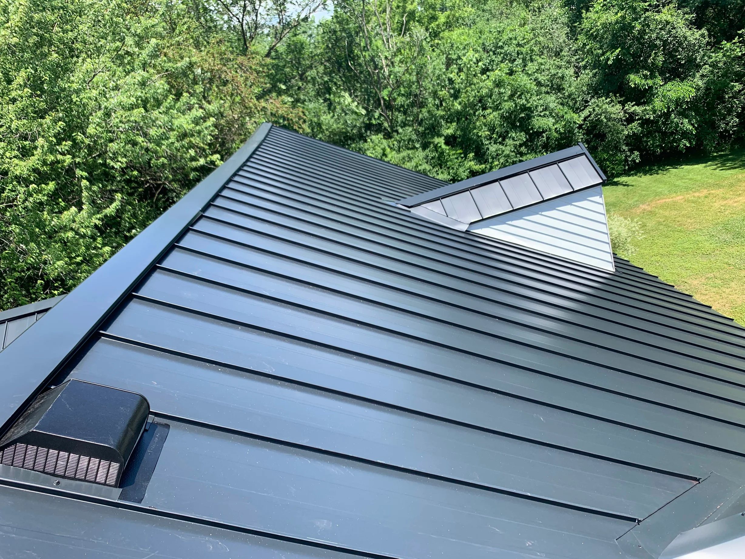 Black Interlock Standing Seam aluminum roof on a black two-storey home with dormers among tall pines, Lake Forest, Illinois