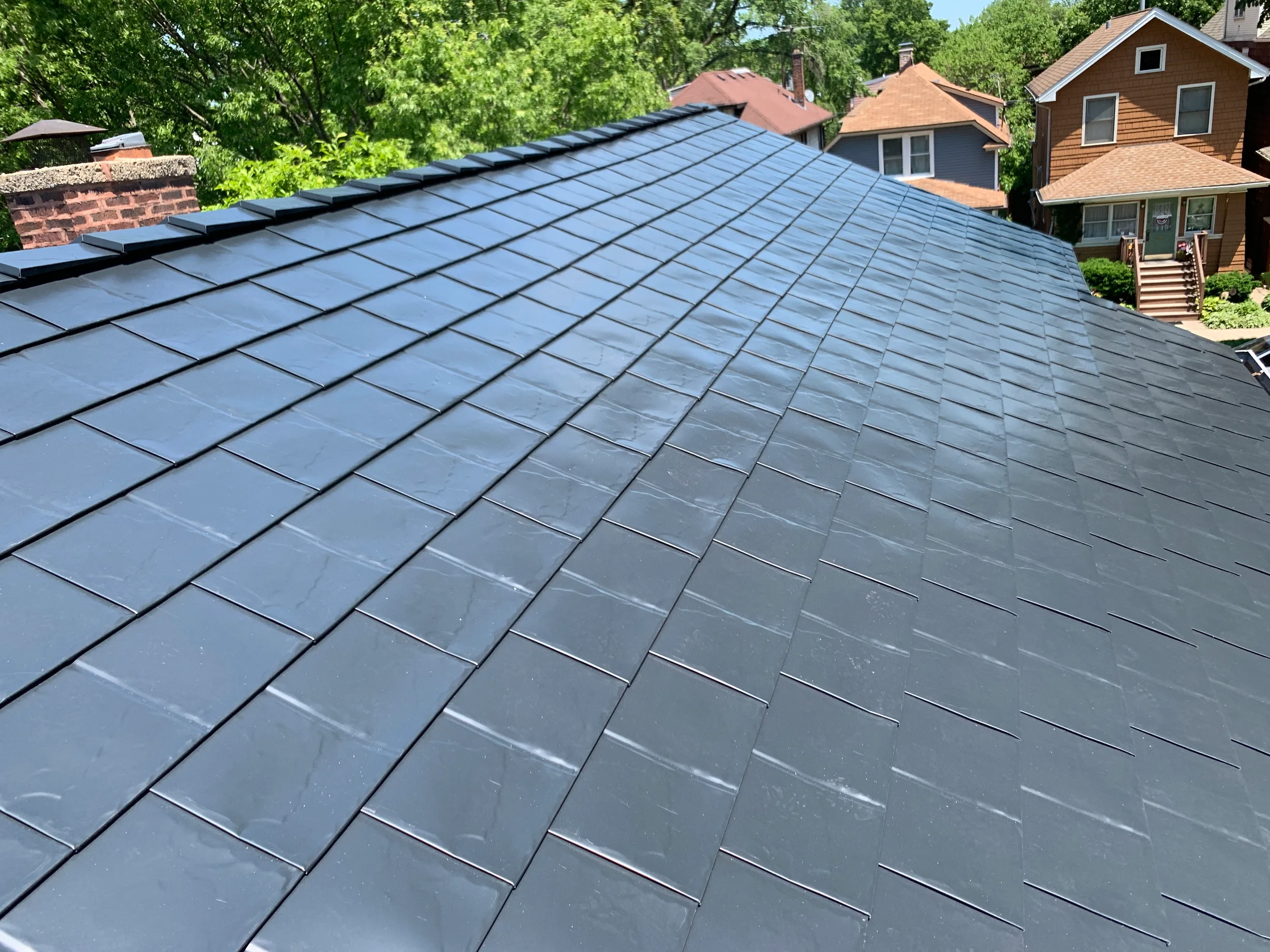 Black Interlock Slate aluminum roof on a brown single-storey home with dormers among tall green, Oak Park, Illinois