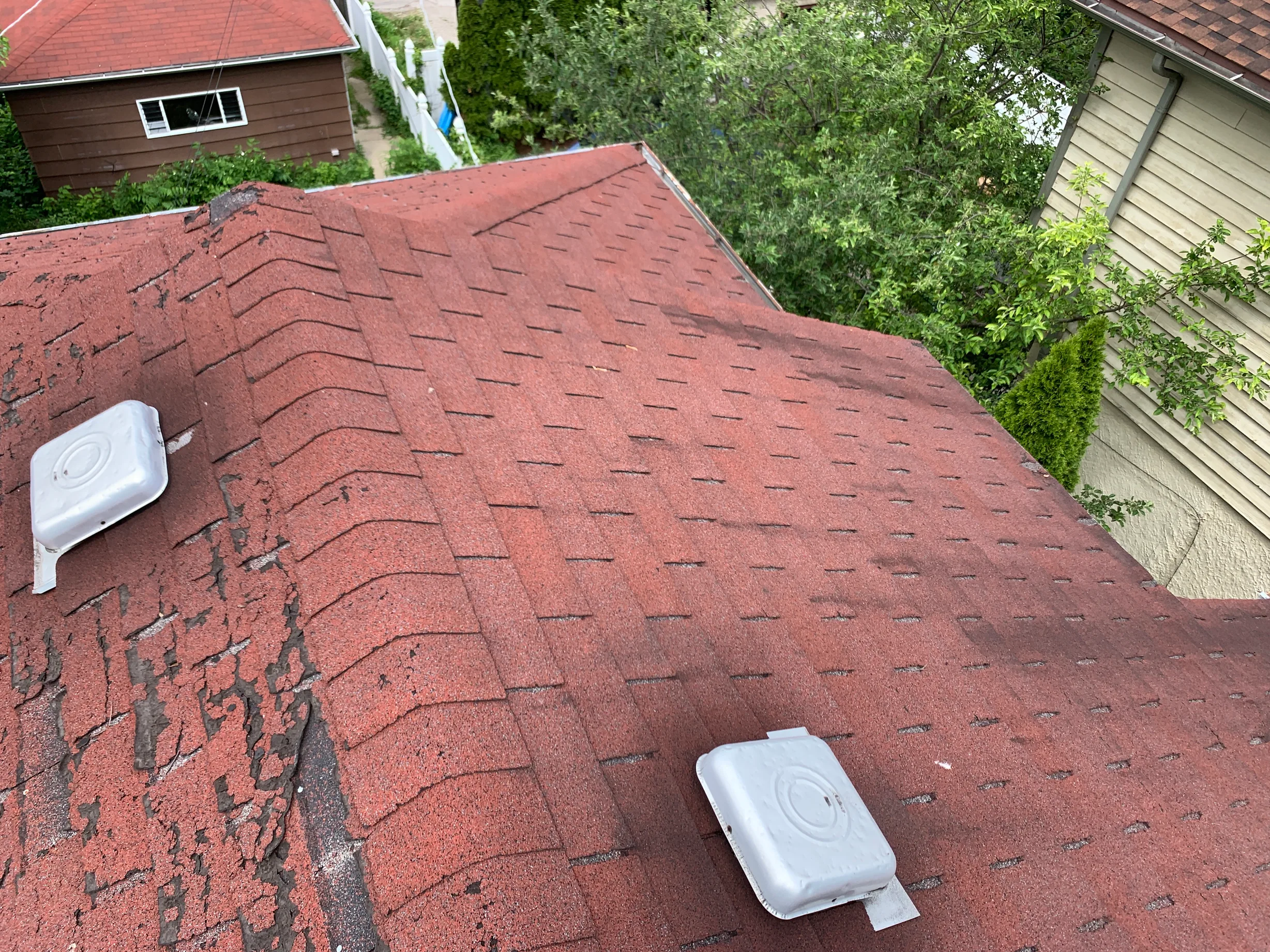 Before: a worn out asphalt shingle roof on a brown house with a red roof among green trees, Oak Park, Illinois, ahead of a Black Interlock Slate aluminum roof