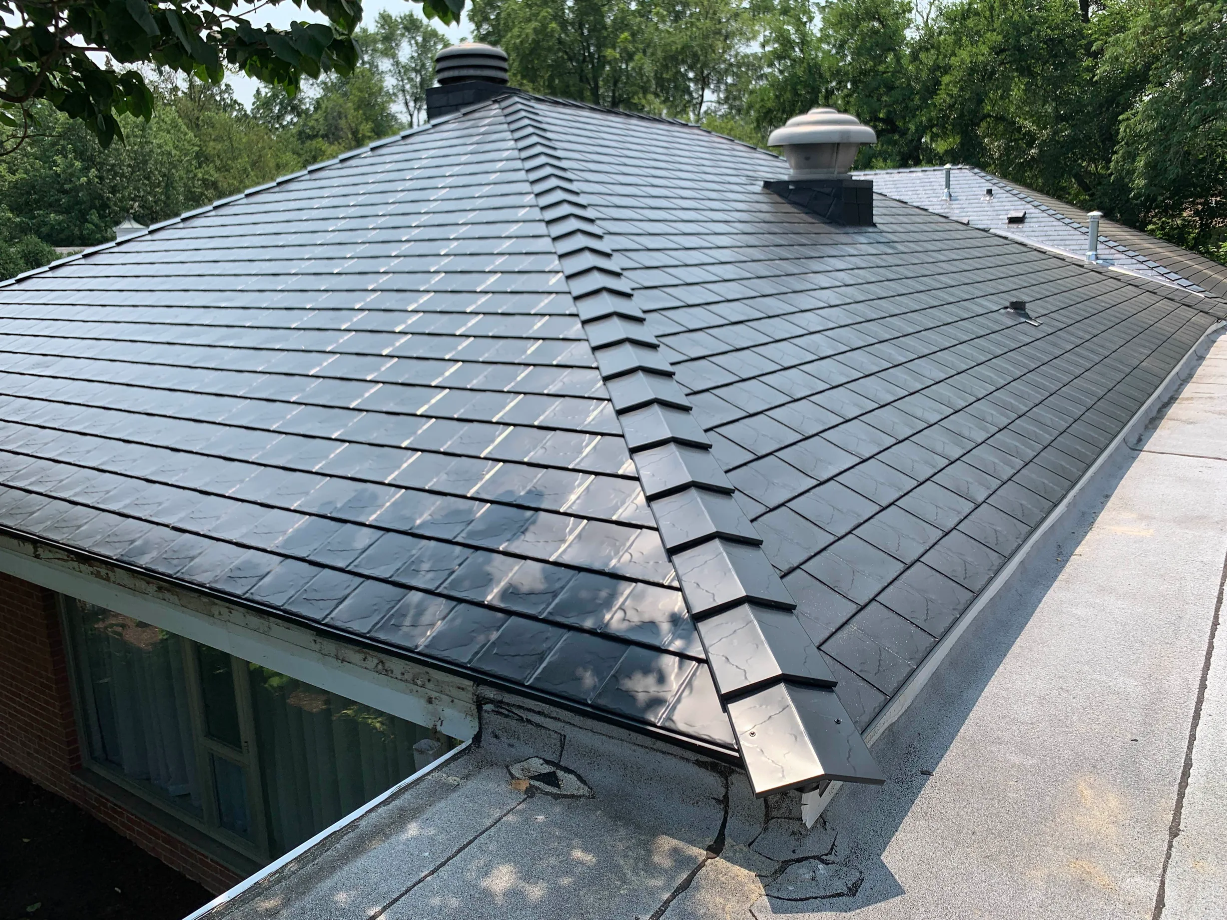 Black Interlock Slate aluminum roof on a brick single-family home with dormers among tall trees, Flossmoor, Illinois