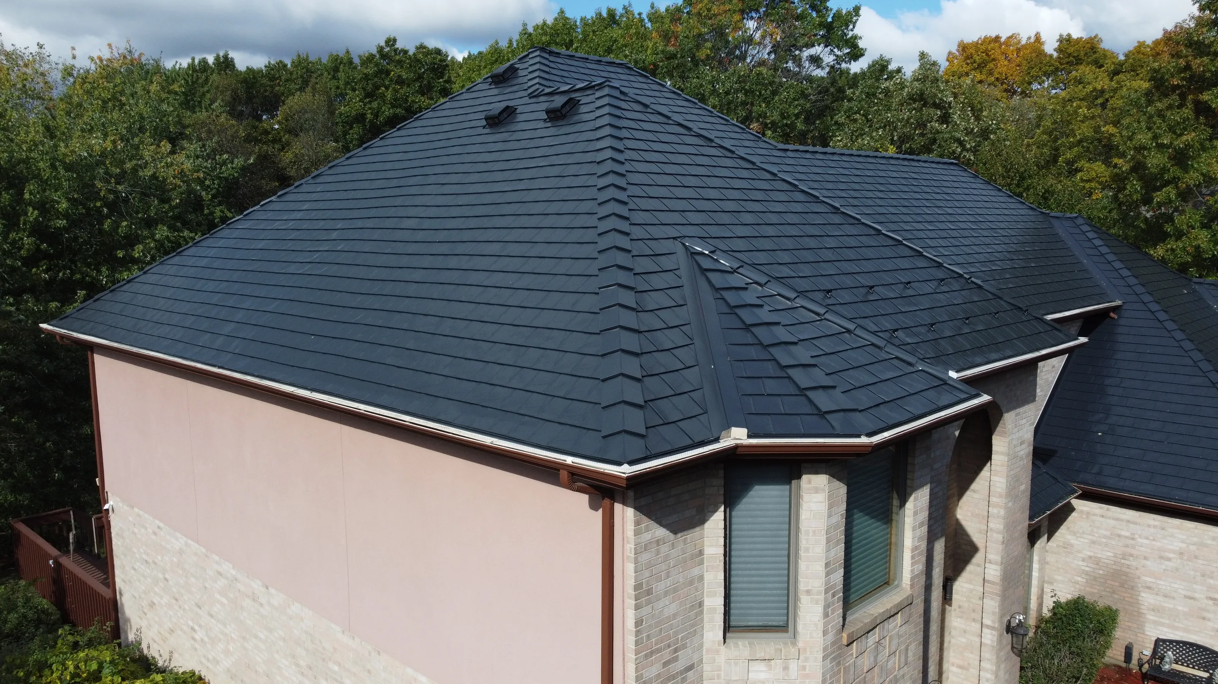 Black Interlock Slate aluminum roof on a beige home with dormers among tall trees and greenery, Lemont, Illinois