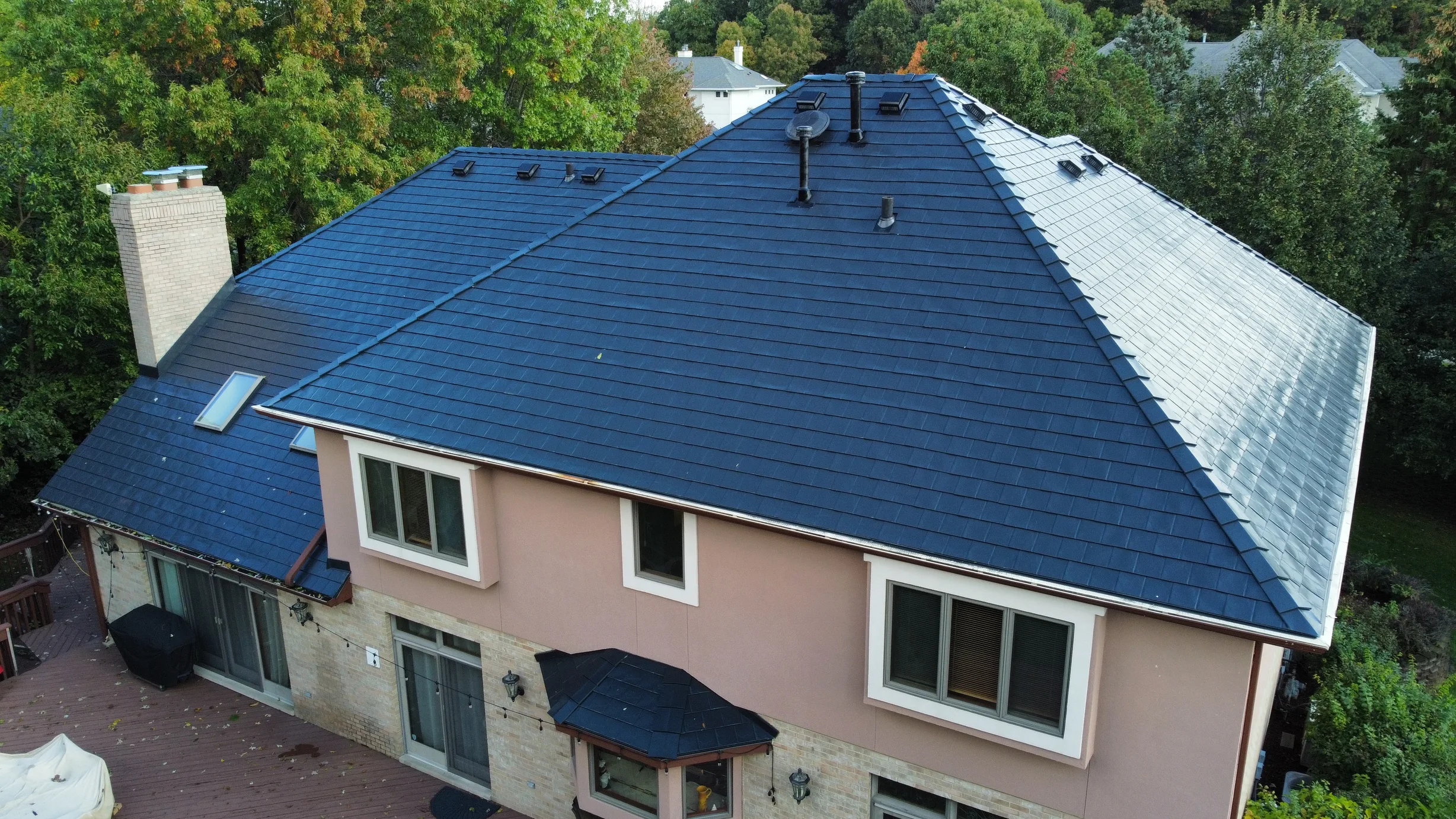 Black Interlock Slate aluminum roof on a tan house with a dark blue metal roof among trees, Lemont, Illinois