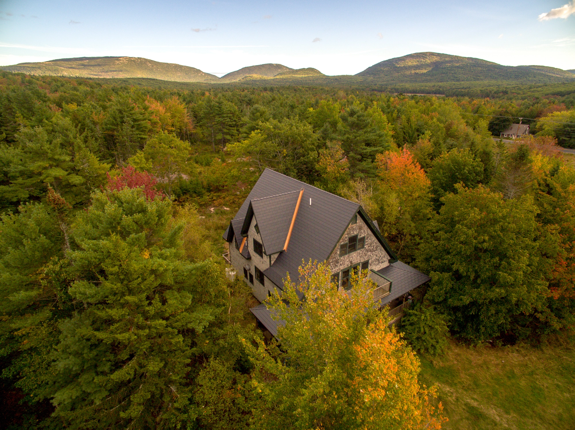 Deep Charcoal Interlock Cedar Shingle aluminum roof on a two-storey home with dormers among tall trees in autumn, Bar Harbor, Maine