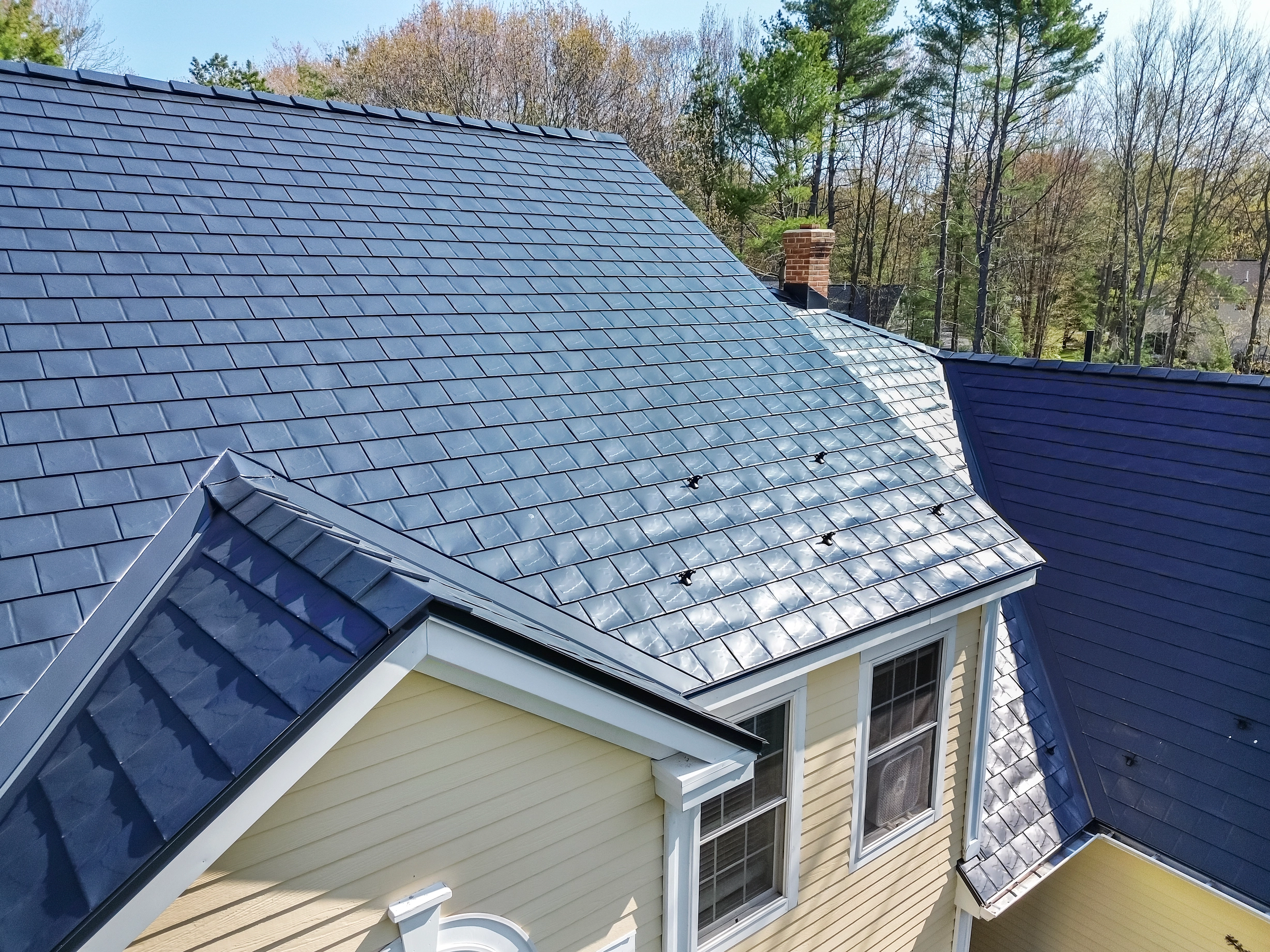 Black Interlock Slate aluminum roof on a yellow house with a metal roof in a forested suburban area, Brunswick, Maine