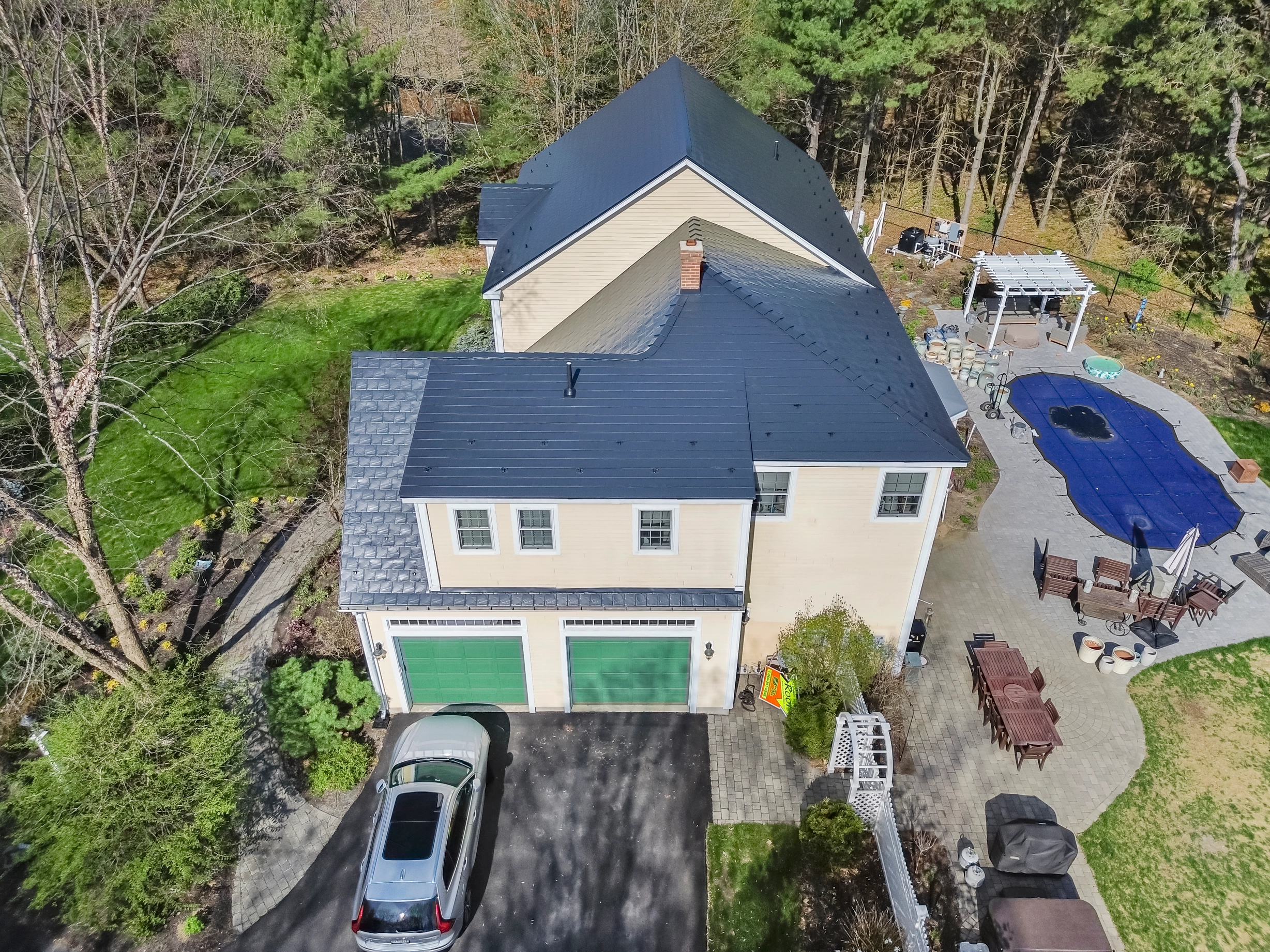 Black Interlock Slate aluminum roof on a beige two-storey home with dormers in a forested setting, Brunswick, Maine