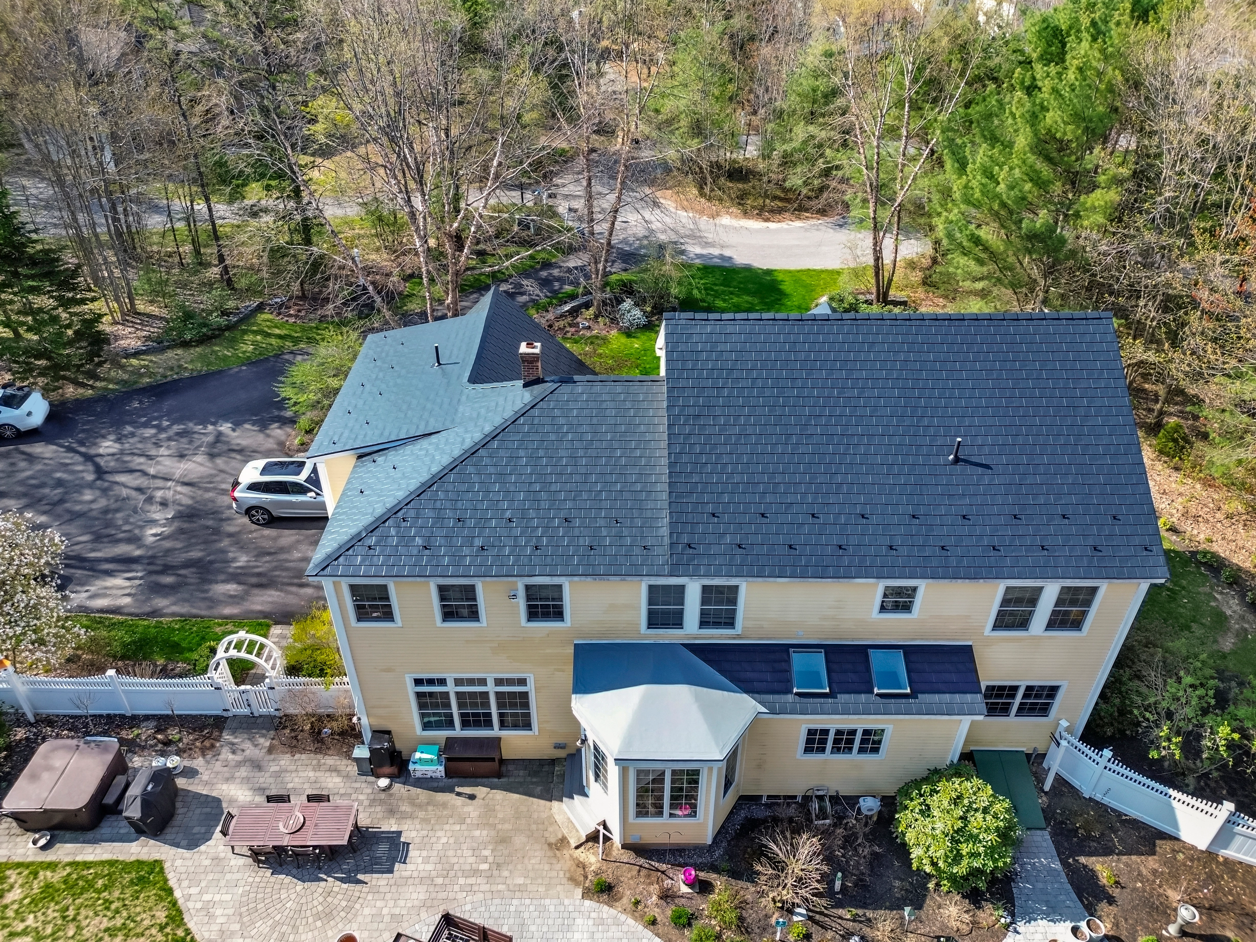 Black Interlock Slate aluminum roof on a two-storey home with a metal roof among tall trees, Brunswick, Maine