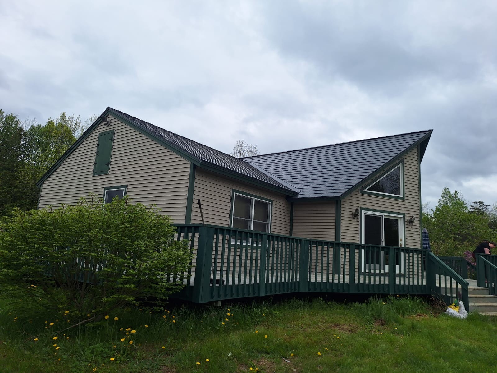1.5-story rural farmhouse with Interlock deep charcoal aluminum slate metal roof, complex multi-plane gable design, tan vinyl siding, and dark green deck in Stetson, ME.