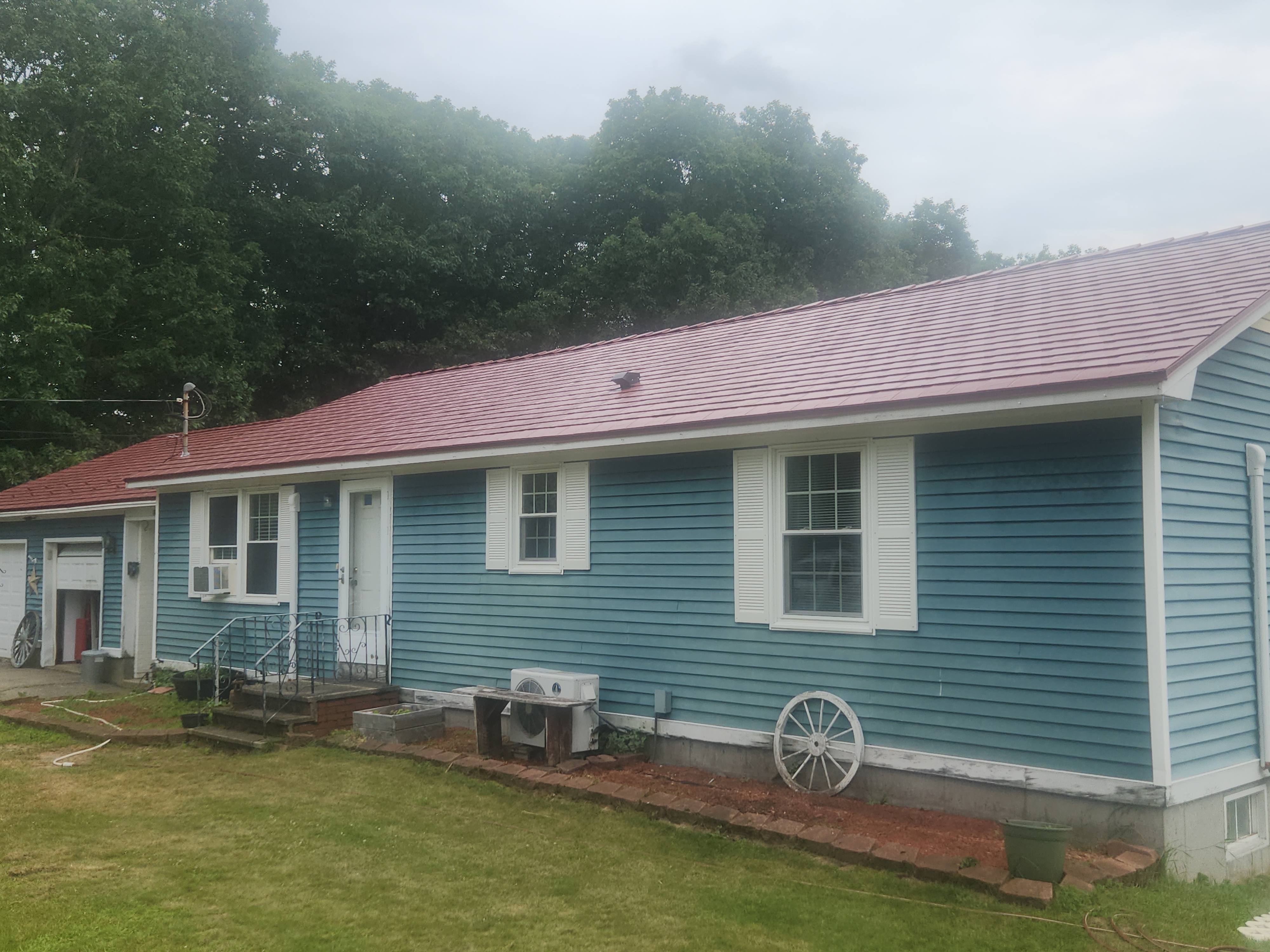 Single-story ranch home with Interlock tile-red aluminum slate metal roof, blue vinyl siding, white shutters, and decorative wagon wheel accents, Lebanon, ME.