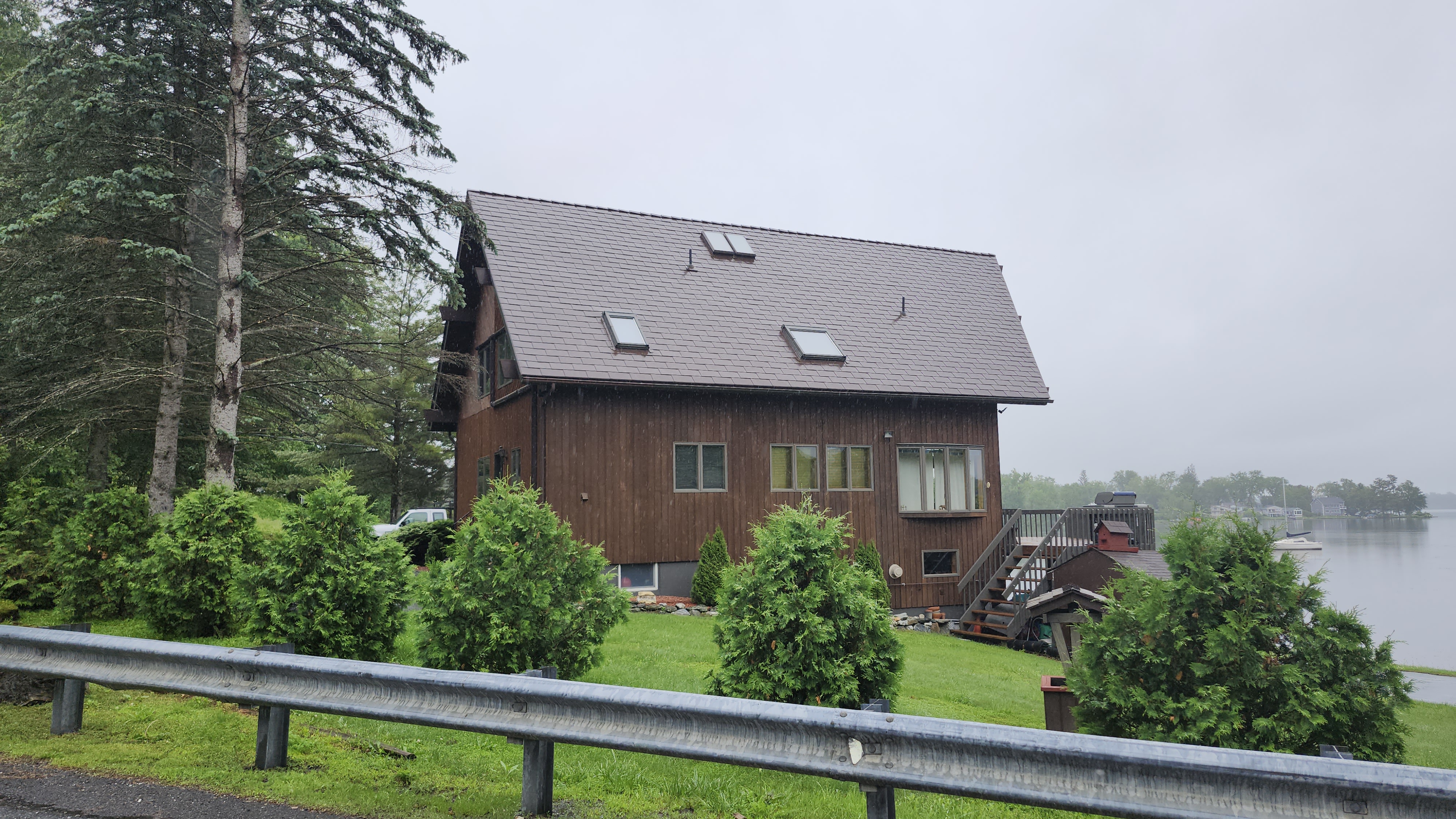 Lakeside chalet-style home with steep Colonial Brown Interlock aluminum shingle roof featuring three skylights, viewed from rear-right elevation on an overcast day.