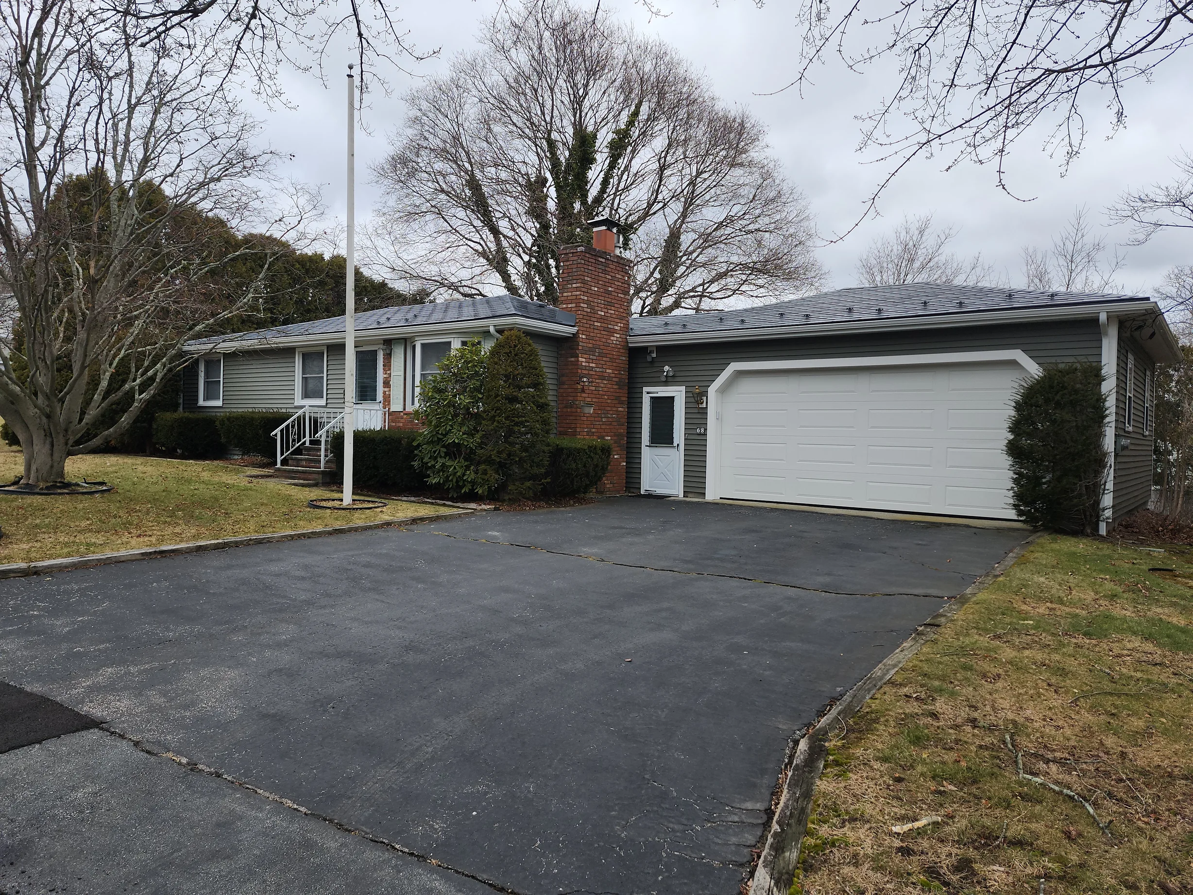 Charcoal Grey Interlock Shingle aluminum roof on a grey single-storey home with garage among bare trees, Somerset, Massachusetts
