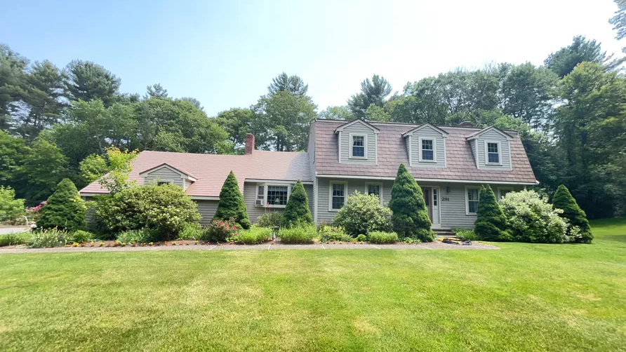 Cape Cod home in Norfolk, MA with Interlock deep charcoal aluminum shingle roof, three dormers, and chimney amid lush green landscaping.