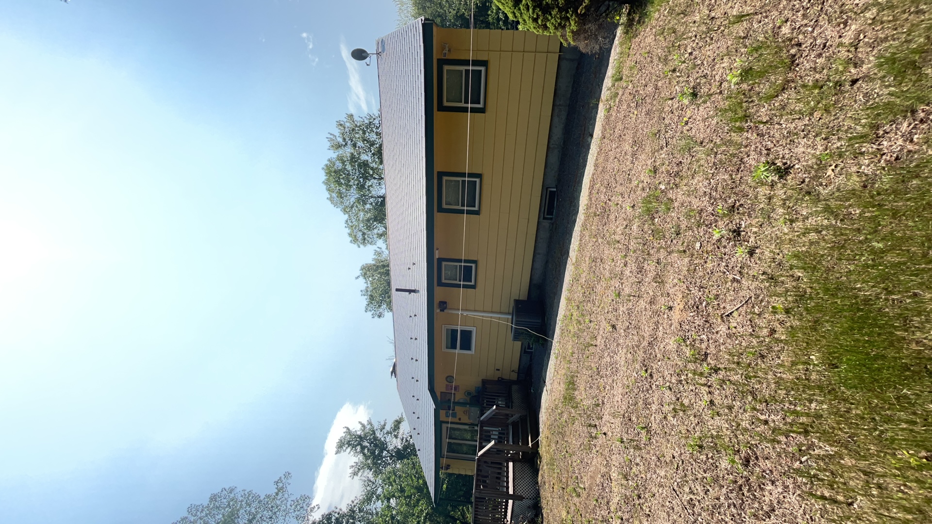 Single-story Ranch home in Norfolk MA with charcoal grey Interlock aluminum slate metal roof, low-pitch gable, yellow siding, and wood deck.
