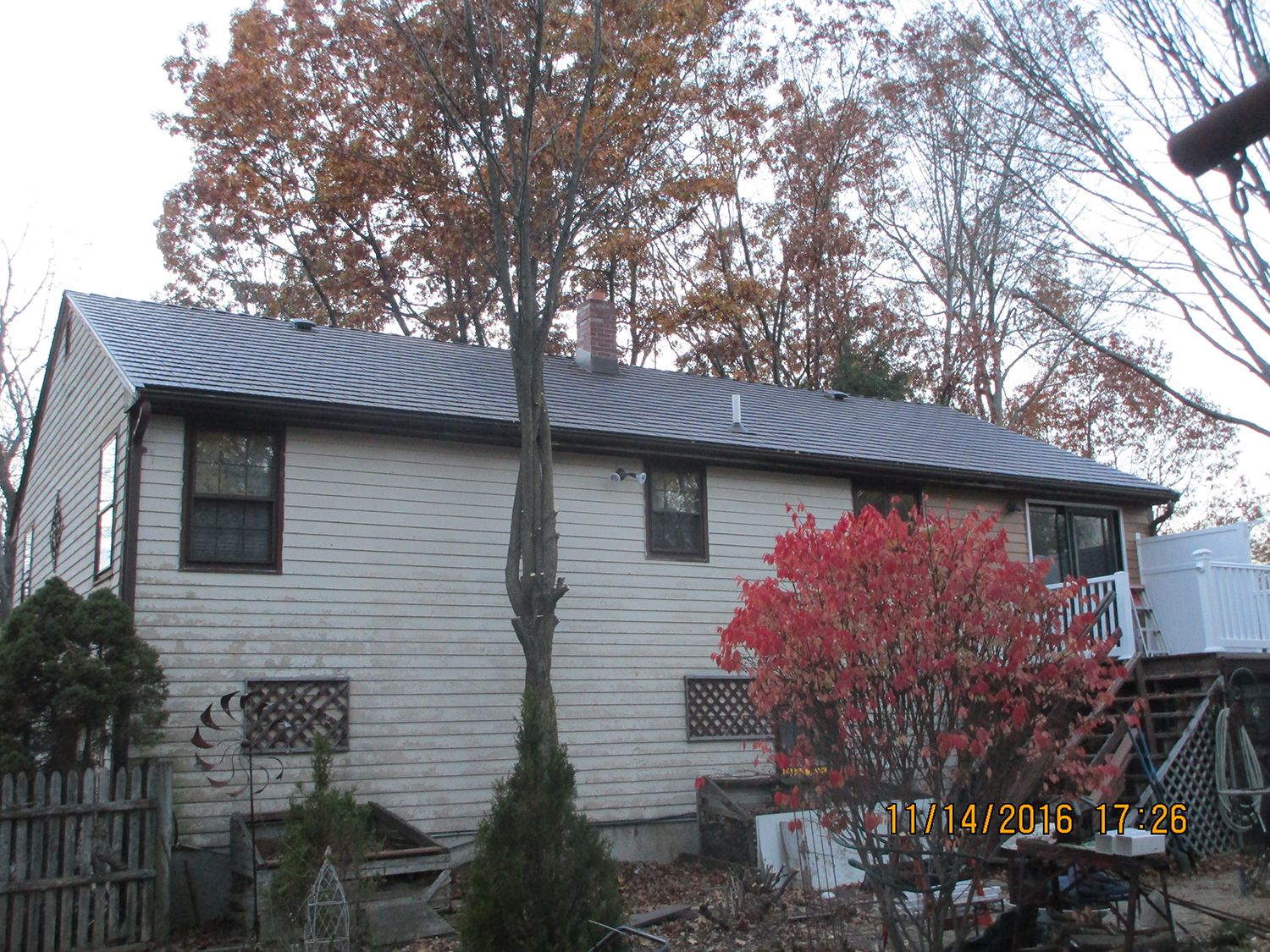 Rear elevation of a 1.5-story home with Interlock Colonial Brown cedar shingle aluminum metal roof, chimney, and gable profile amid fall foliage.