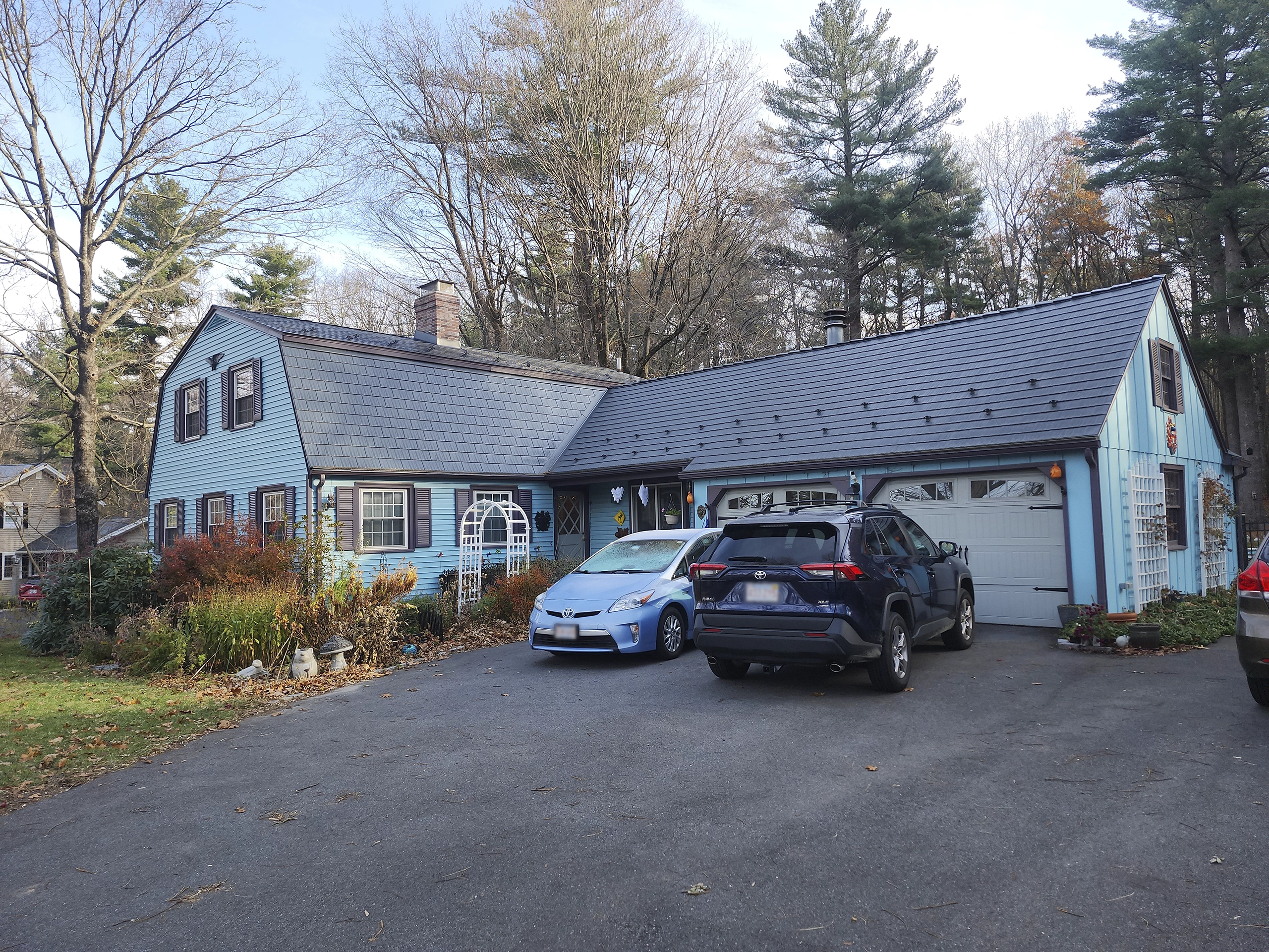 Gambrel-style colonial home with Interlock deep charcoal cedar shingle metal roofing, chimney, and attached garage in a forested Westborough, MA suburb.