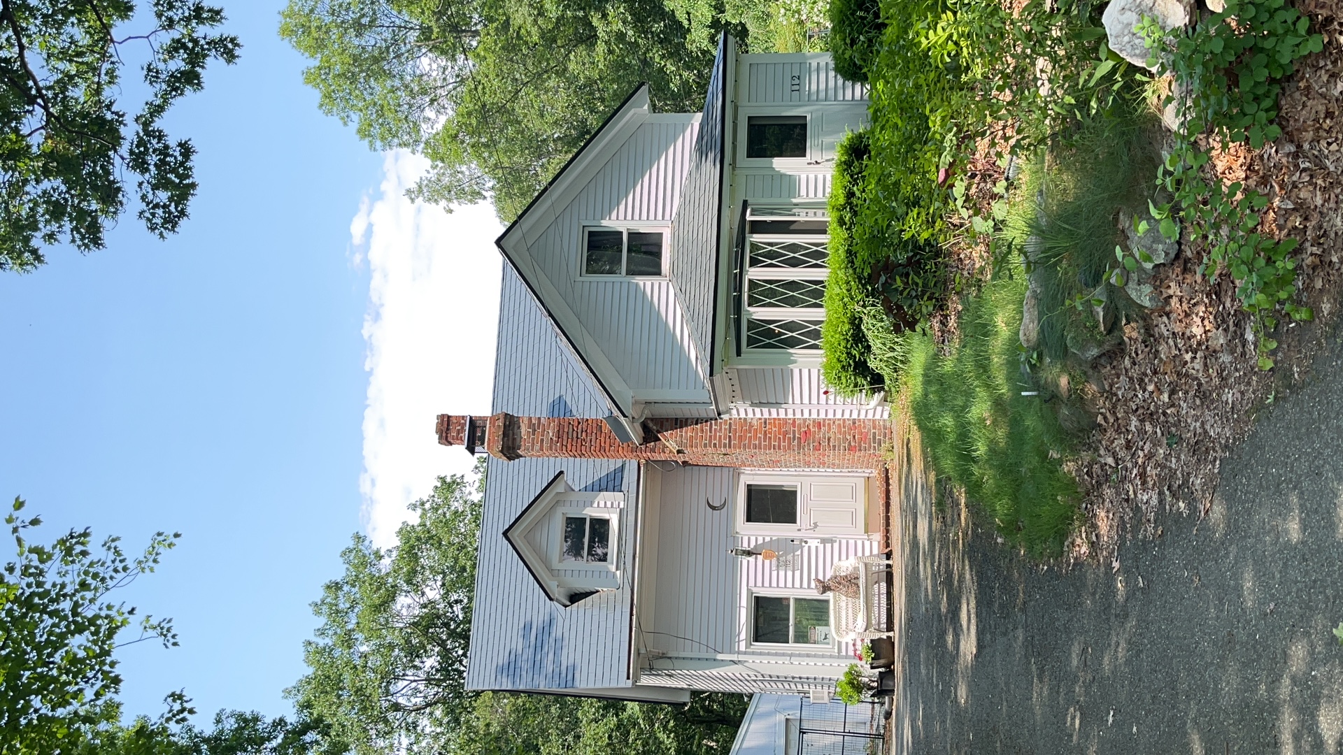 Cape Cod home in Wrentham MA with Interlock deep charcoal aluminum slate roof, prominent brick chimney, and two dormers surrounded by mature trees.