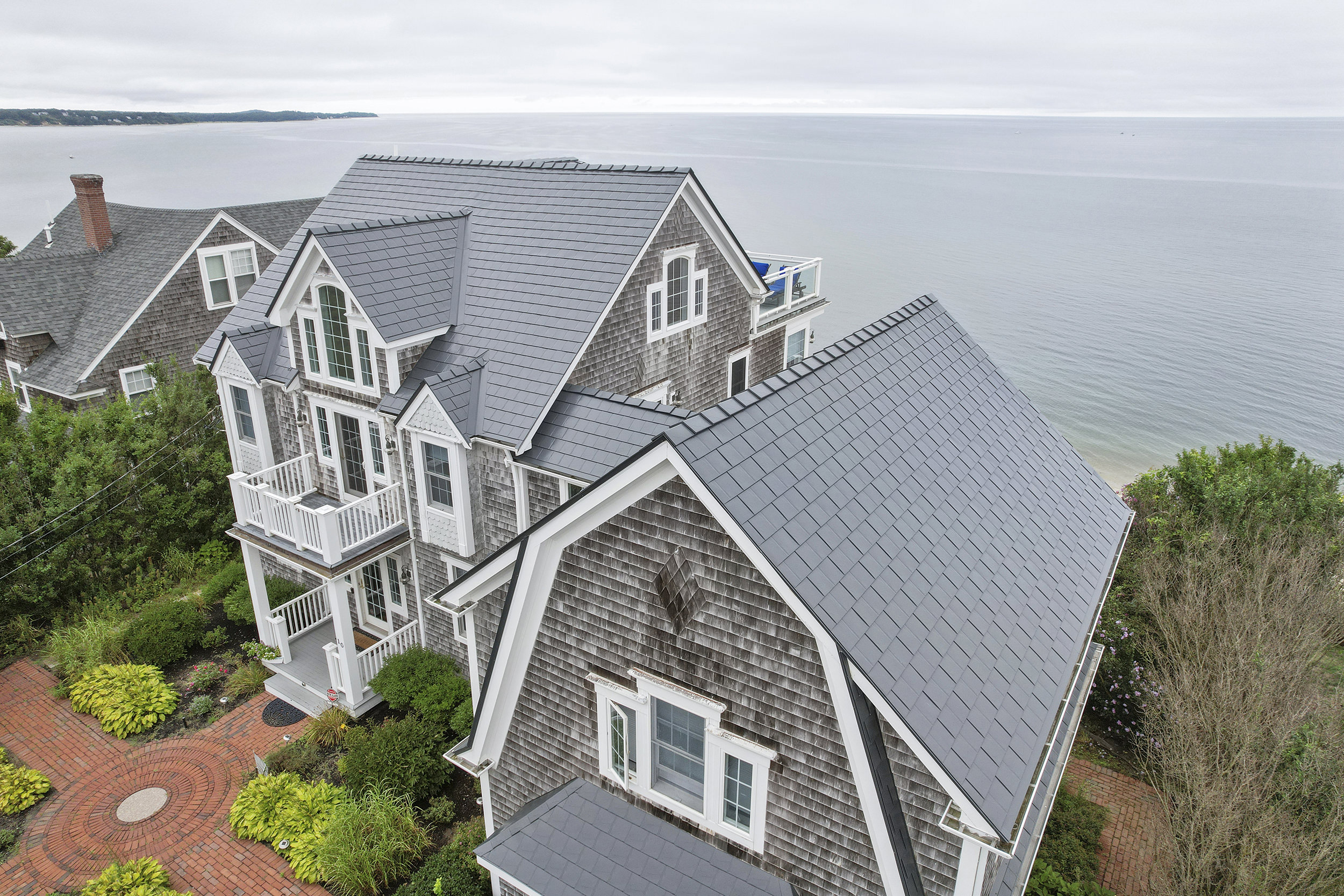 Aerial view of a large coastal shingle-style home in Sagamore Beach, MA featuring a complex Deep Charcoal Interlock aluminum slate metal roof with multiple dormers and valleys.