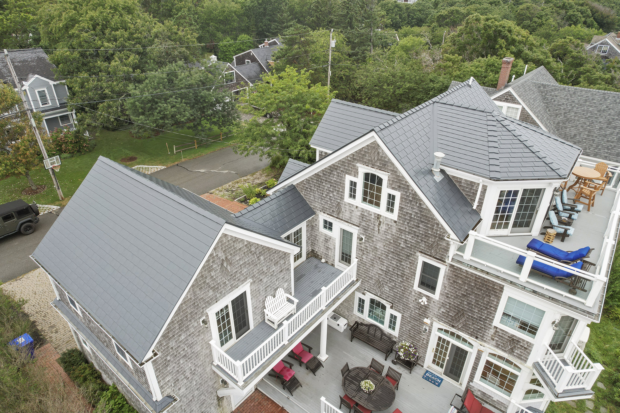 Aerial rear view of a large Craftsman-style coastal home in Sagamore Beach, MA with a complex multi-hip Deep Charcoal aluminum slate metal roof featuring multiple dormers and valleys.