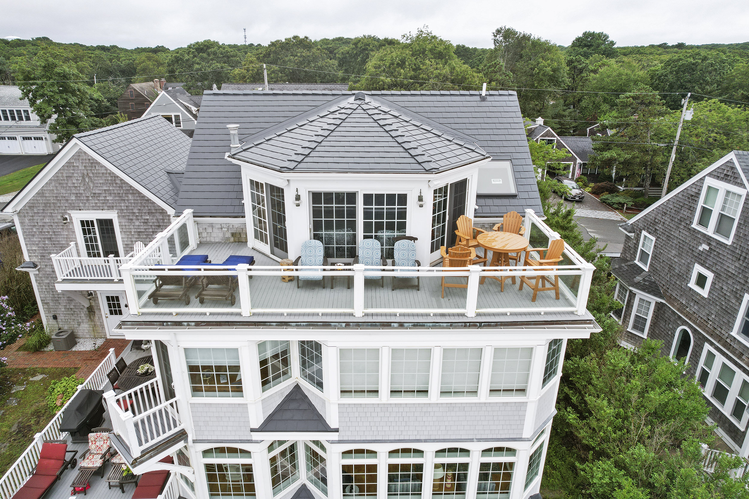 Aerial front view of a 3-story coastal shingle-style home in Sagamore Beach, MA featuring a multi-hip Interlock aluminum slate roof in Deep Charcoal with a rooftop deck.