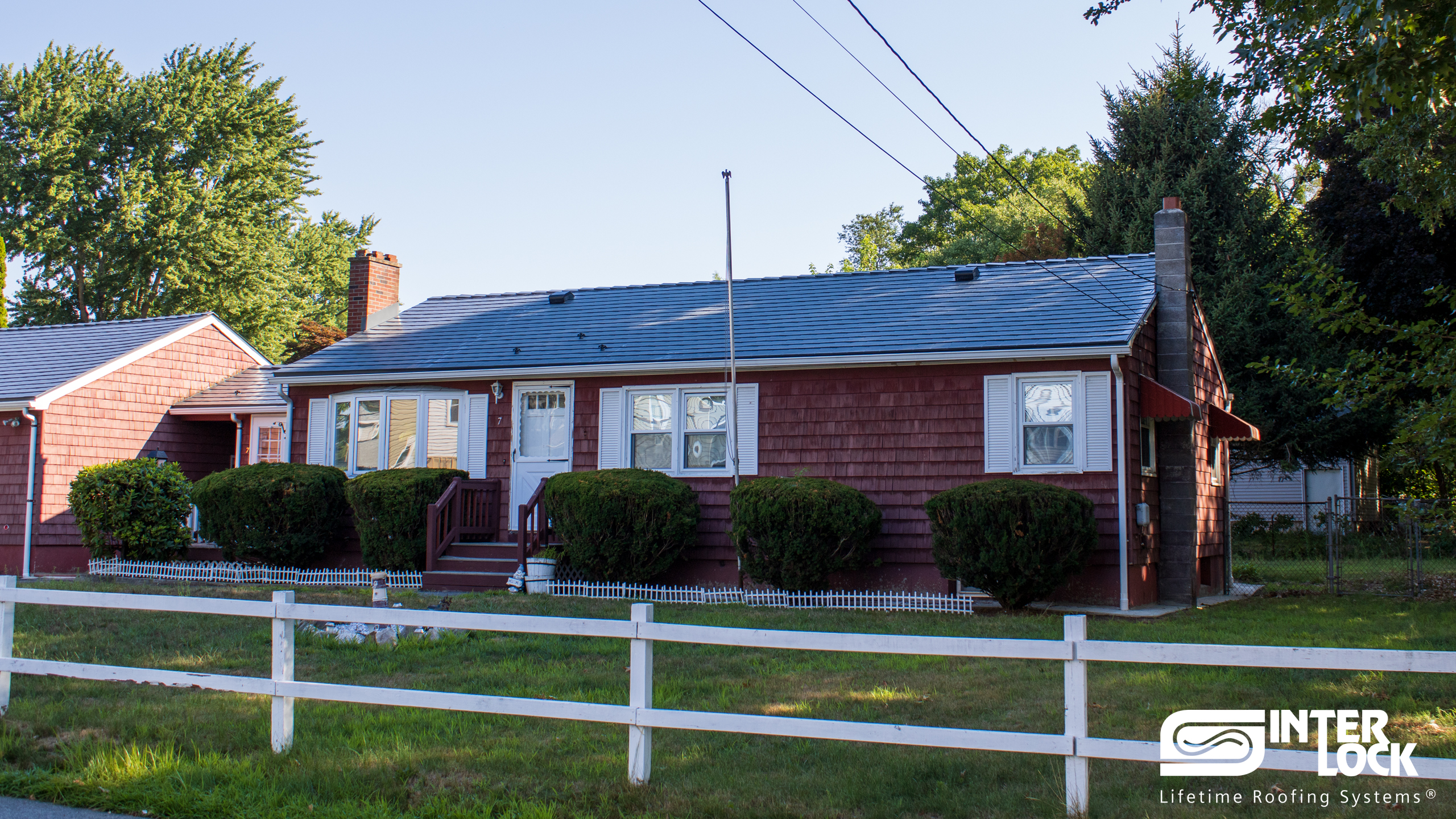 Single-story ranch home with Interlock deep charcoal aluminum slate metal roof, red cedar shingle siding, white trim, and brick chimneys in Wilbraham, MA.