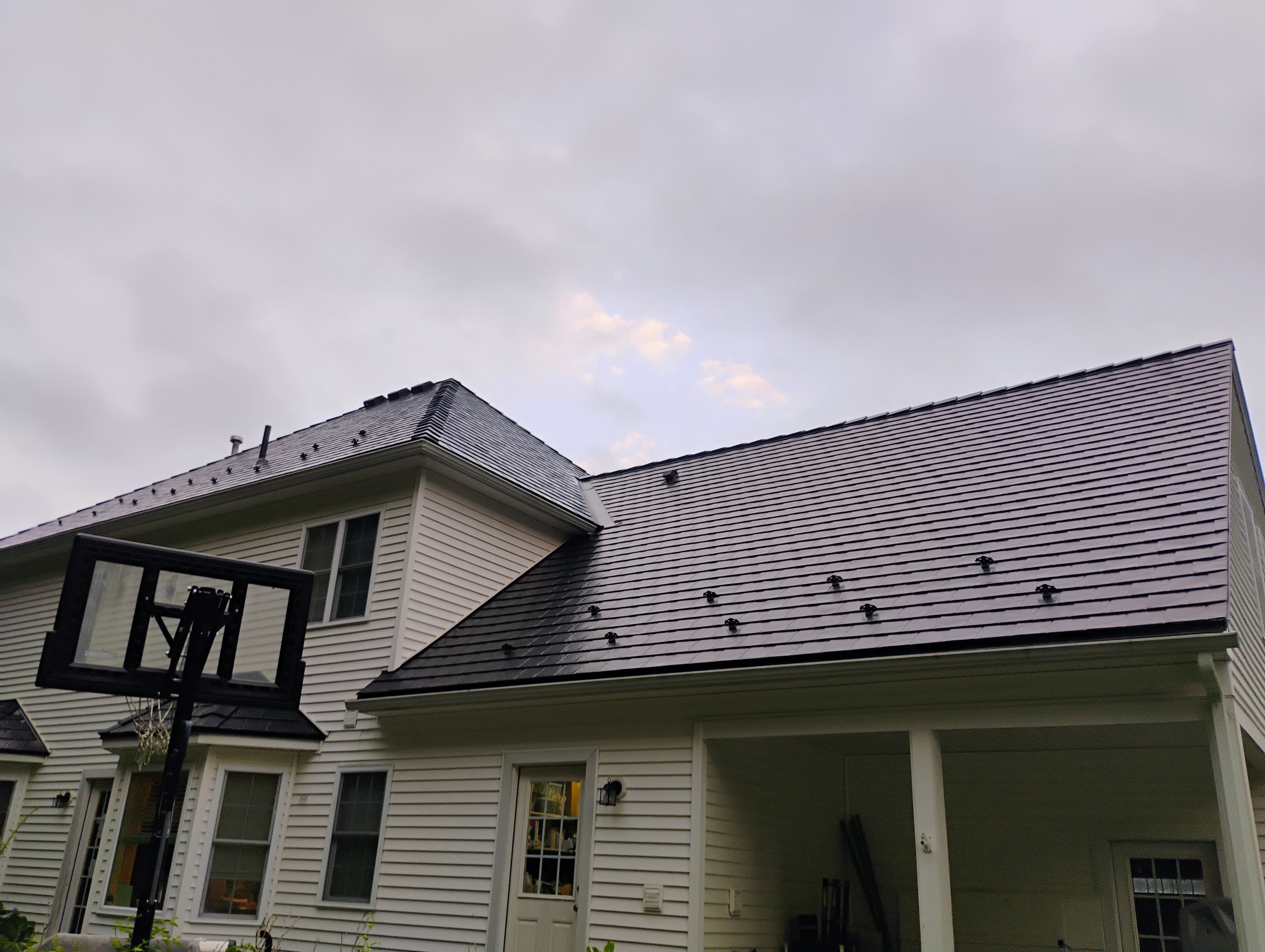 Two-story Colonial home with a complex black Interlock aluminum slate metal roof featuring snow guards, a dormer, and covered rear porch.
