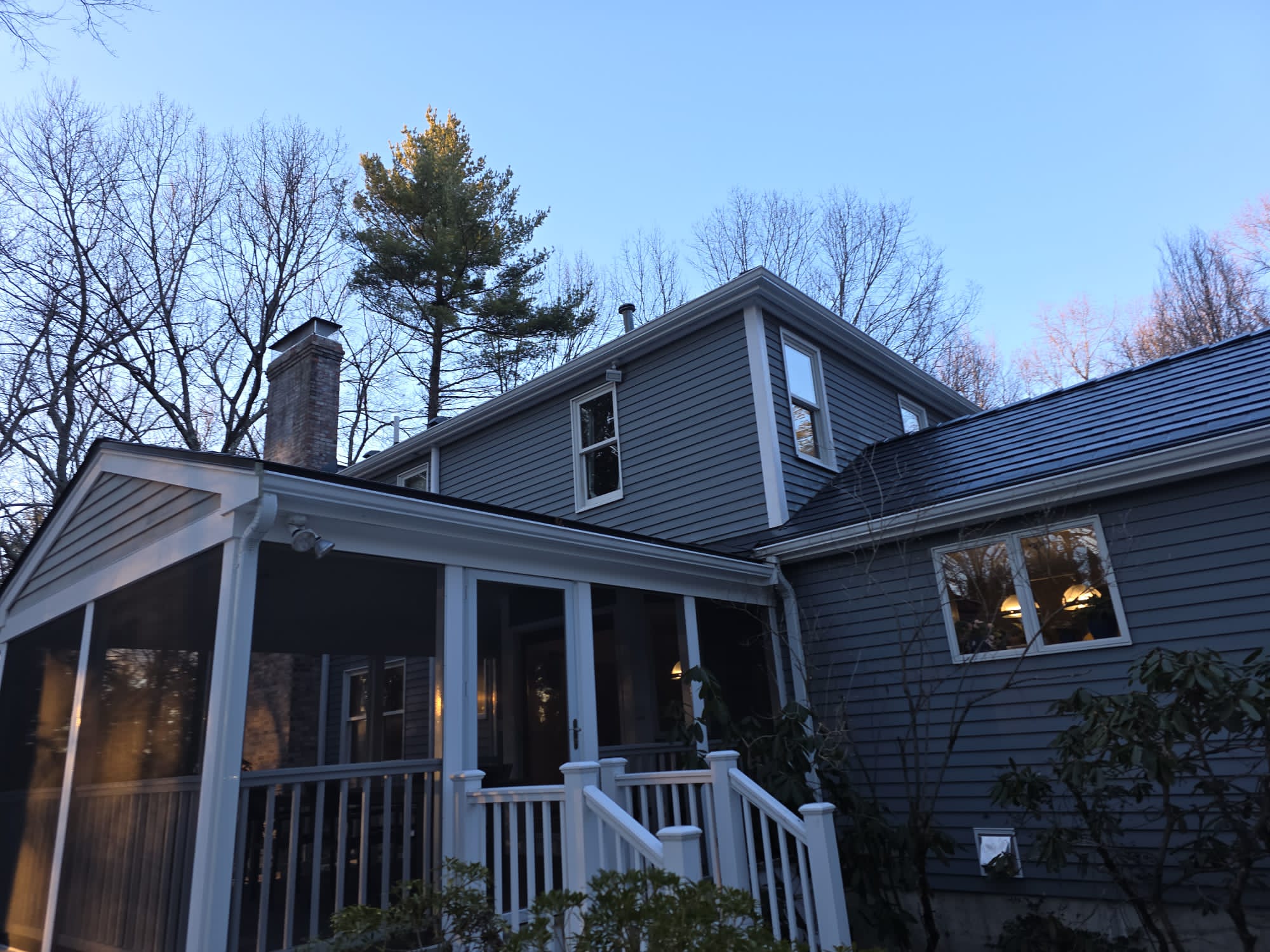 Rear-left view of a two-story colonial home in Westford, MA with Interlock deep charcoal aluminum slate roofing, dormer, and chimney at dusk.