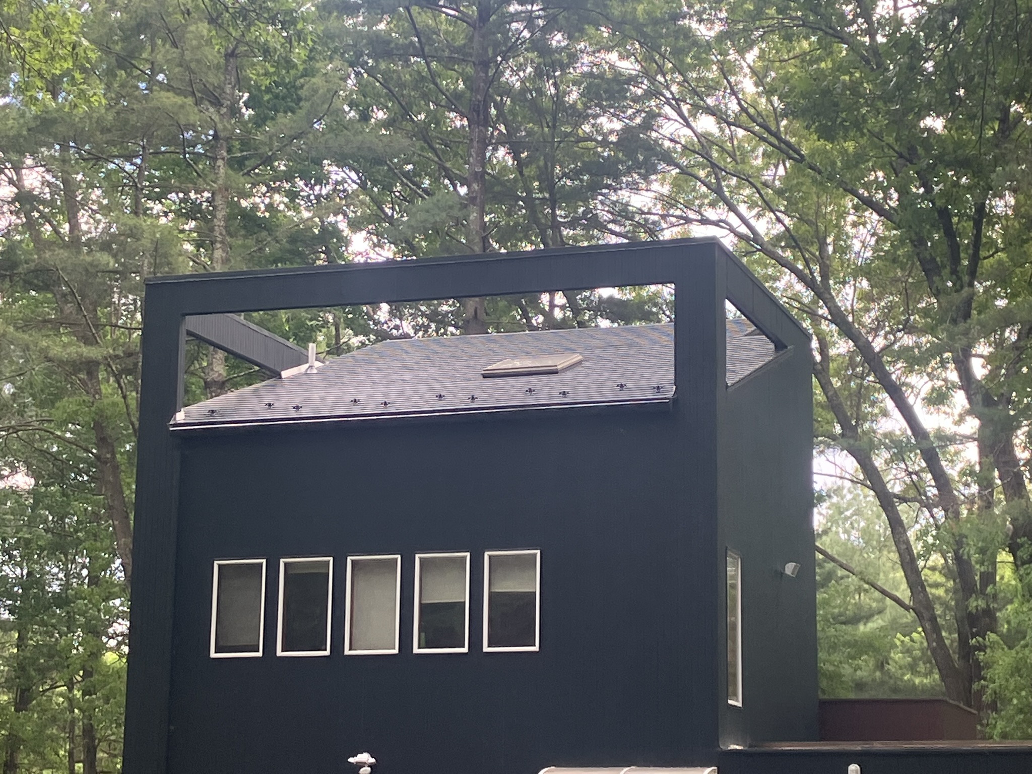 Modern black two-story home with Interlock deep charcoal aluminum slate roof, skylight, and vent pipe visible above a row of horizontal windows, surrounded by forest.