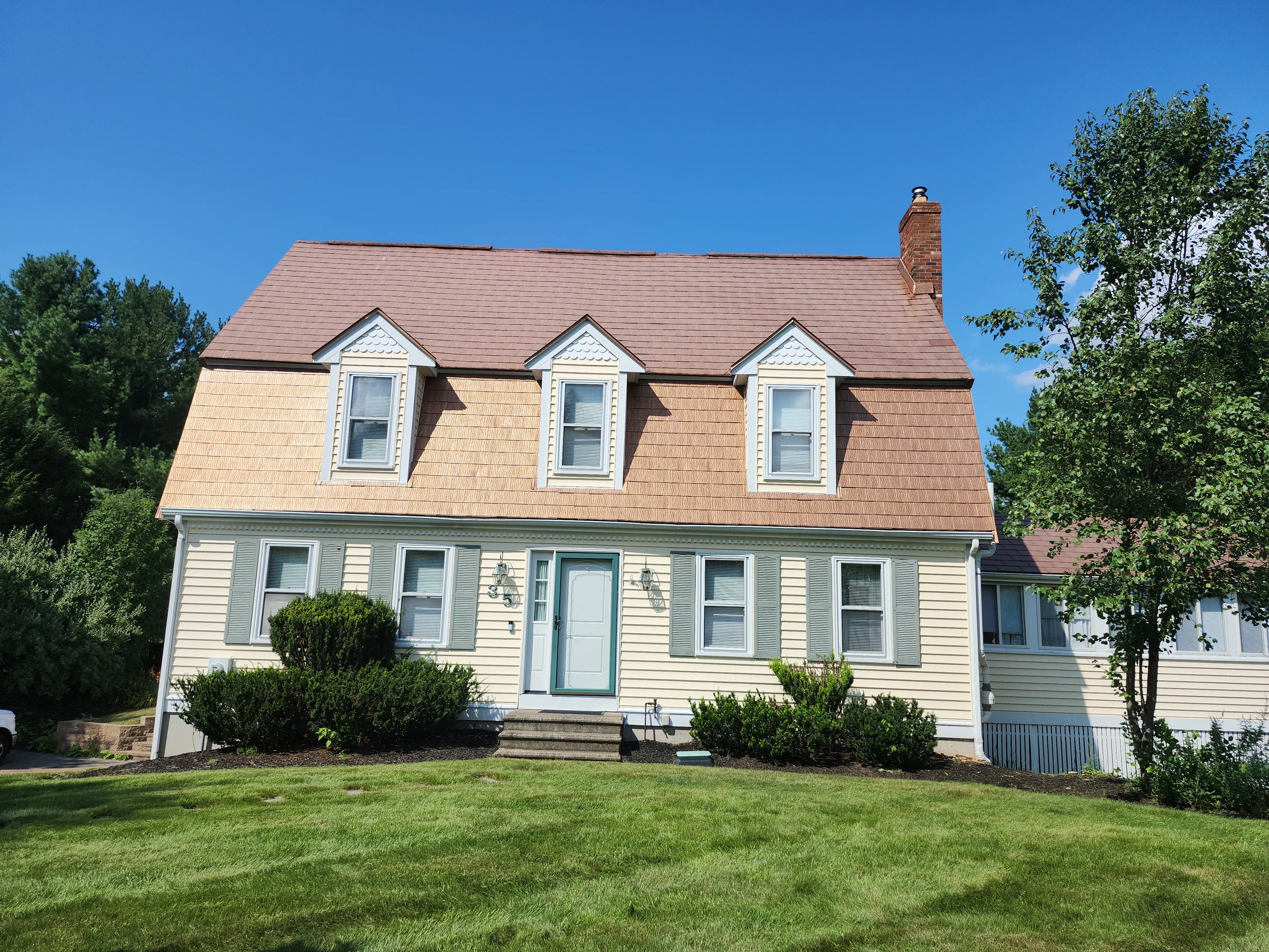 Aged Copper Interlock Shingle aluminum roof on a yellow two-storey Colonial home with dormers among tall, Wrentham, Massachusetts