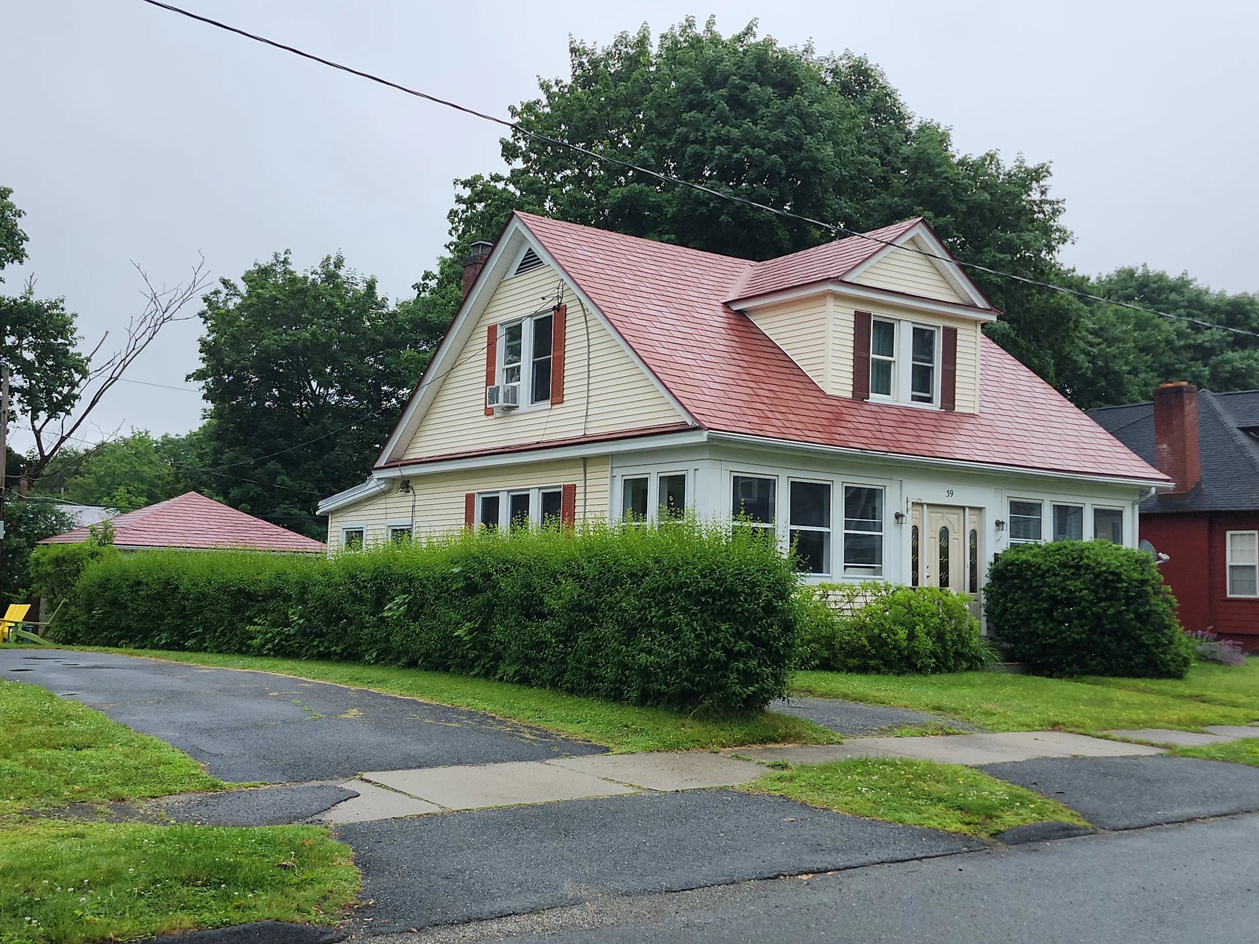 Tile Red Interlock Shingle aluminum roof on a cream and red two-storey home with dormers among tall, Pittsfield, Massachusetts