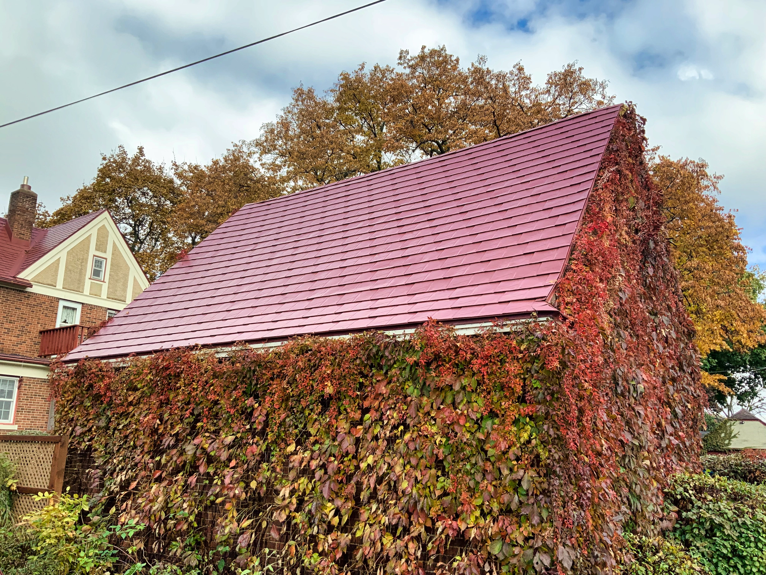 Tile Red Interlock Tile aluminum roof on a brick two-storey home with dormers among tall trees, Saint Paul, Minnesota