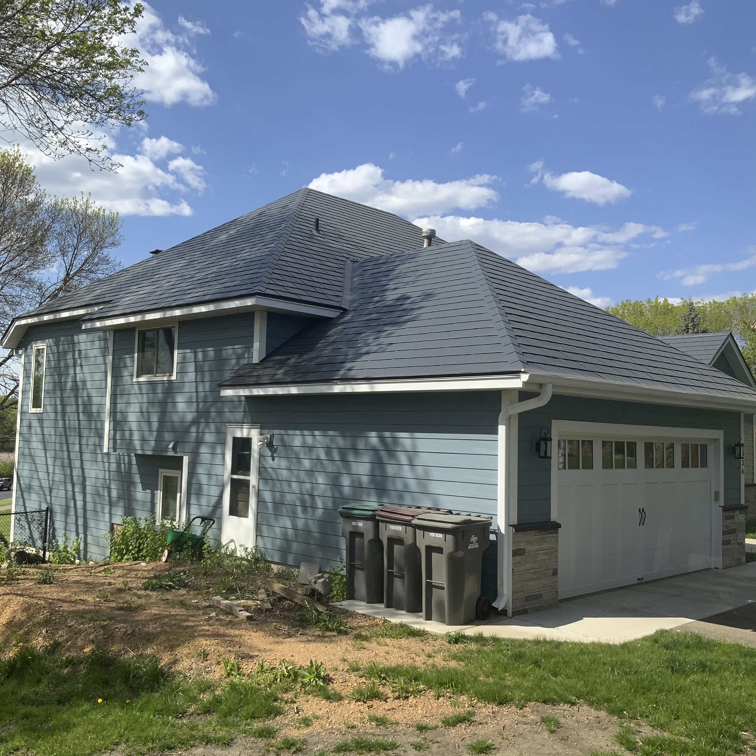 Two-story suburban home with charcoal grey Interlock aluminum slate metal roofing on a complex multi-hip profile, blue lap siding, and attached garage.