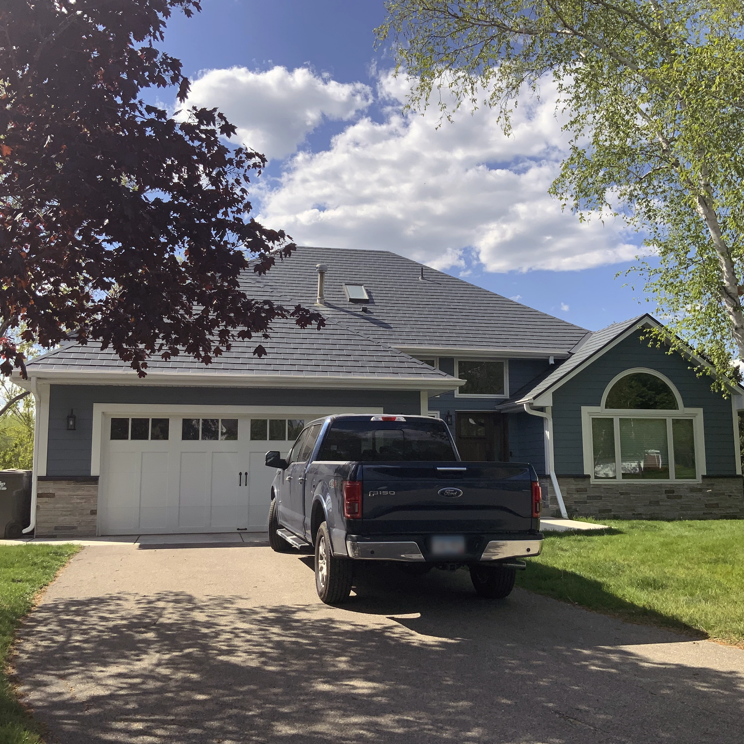 Charcoal grey Interlock aluminum slate metal roof on a blue Craftsman-style home in Eden Prairie, MN, featuring a skylight and multi-hip roofline.
