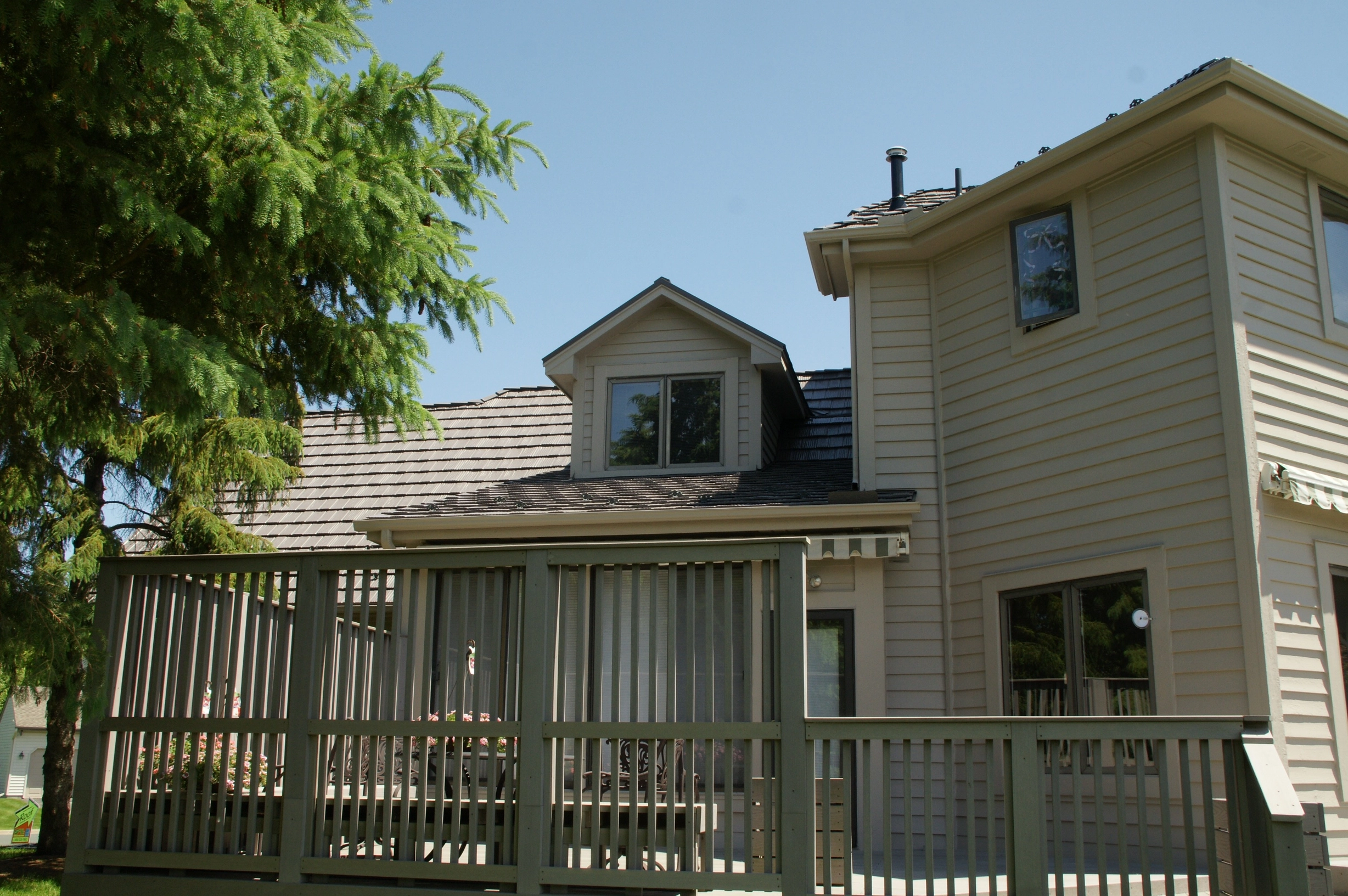 Weathered Interlock Shake aluminum roof on a beige modern home with a large deck among tall green trees, Mendota Heights, Minnesota