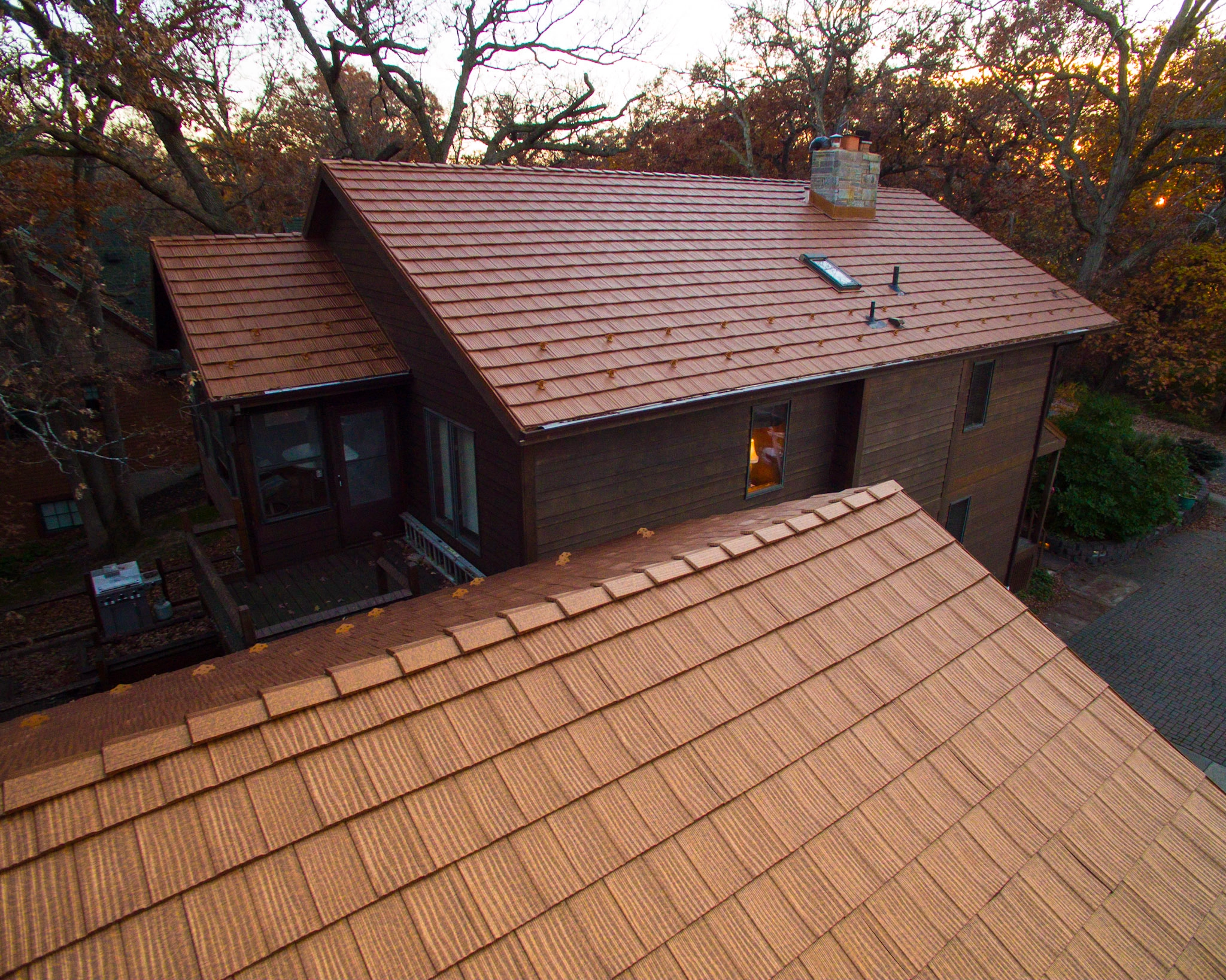 Aged Copper Interlock Shake aluminum roof on a two-storey home with dormers among tall trees, Bloomington, Minnesota