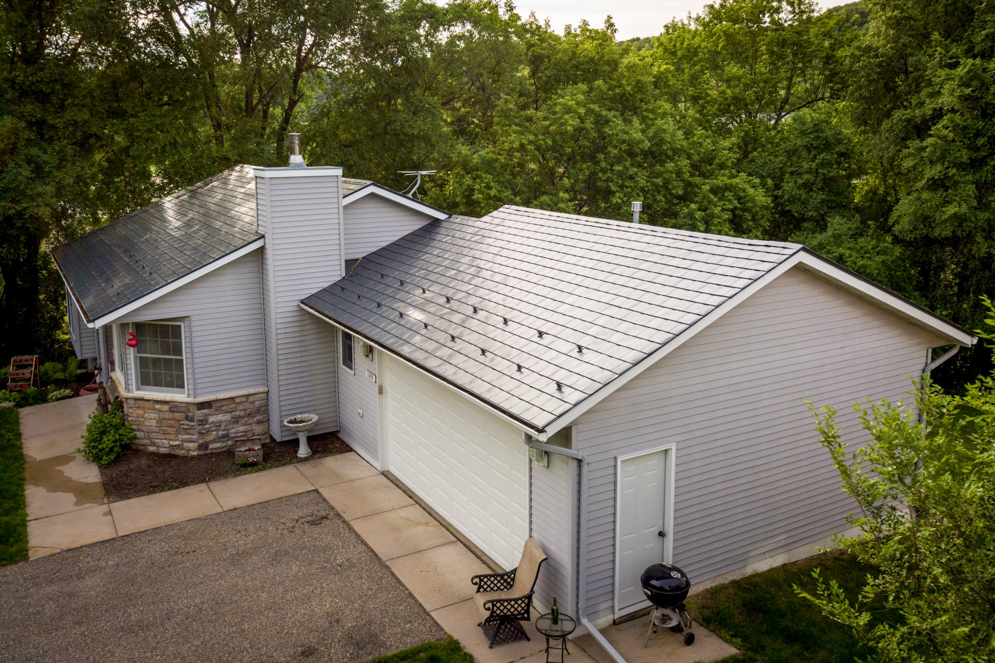 Deep Charcoal Interlock Slate aluminum roof on a white ranch home with a metal roof among tall trees, Red Wing, Minnesota