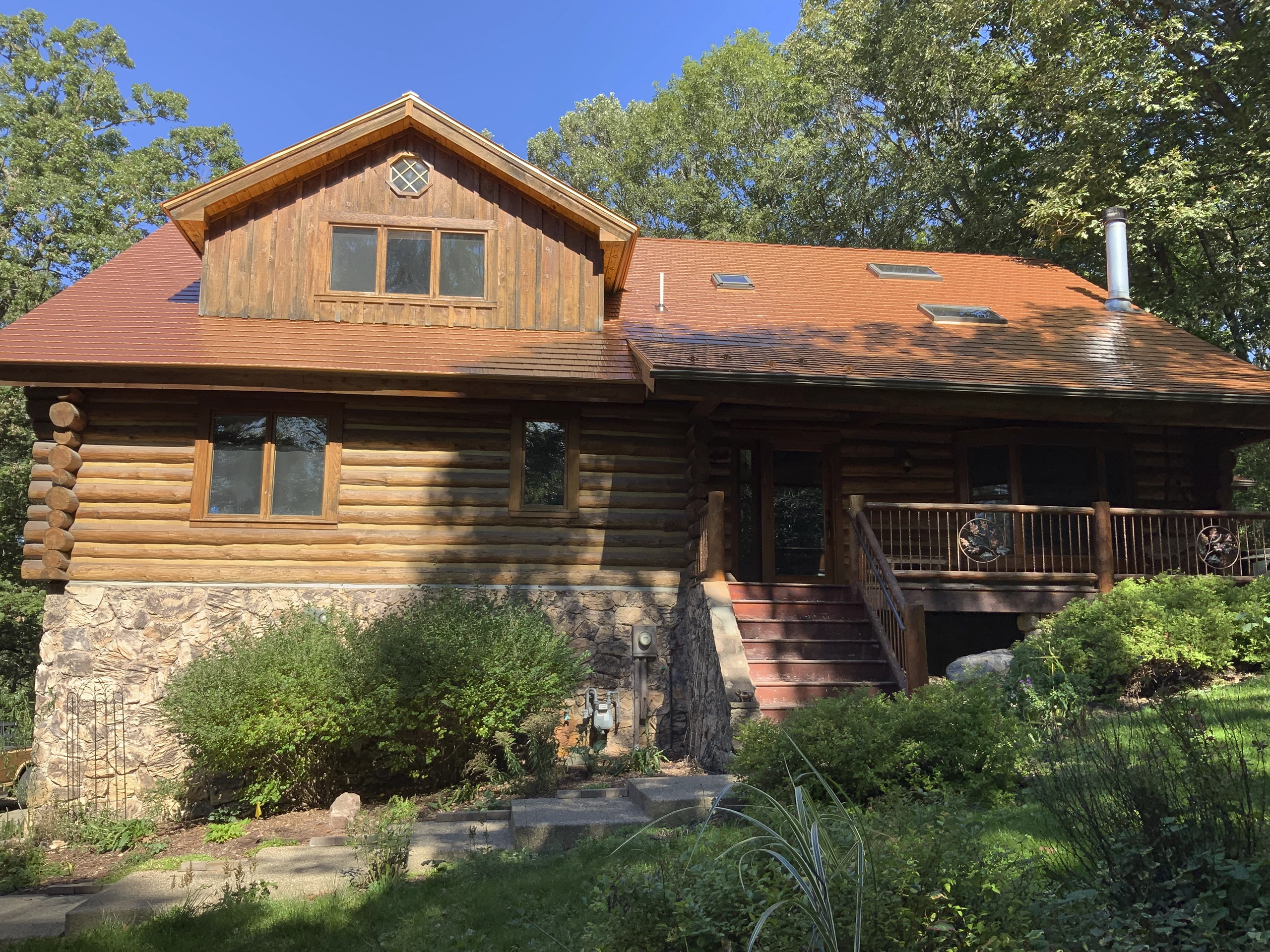 Log-and-stone craftsman home in Lakeville MN with Interlock Copper Penny cedar shingle metal roof, dormer, skylights, and wraparound deck.