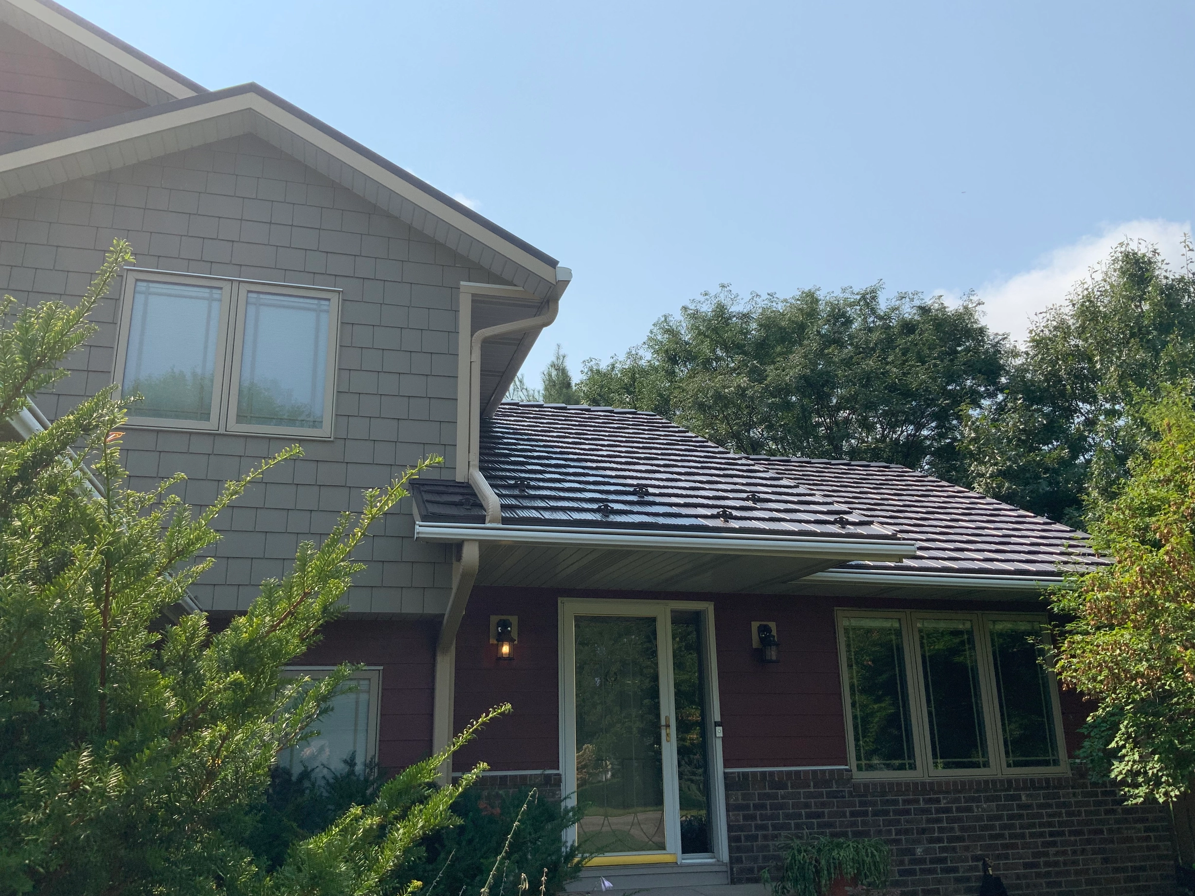 Tudor Brown Interlock Shake aluminum roof on a brown two-storey home with a metal roof in a forest, Northfield, Minnesota