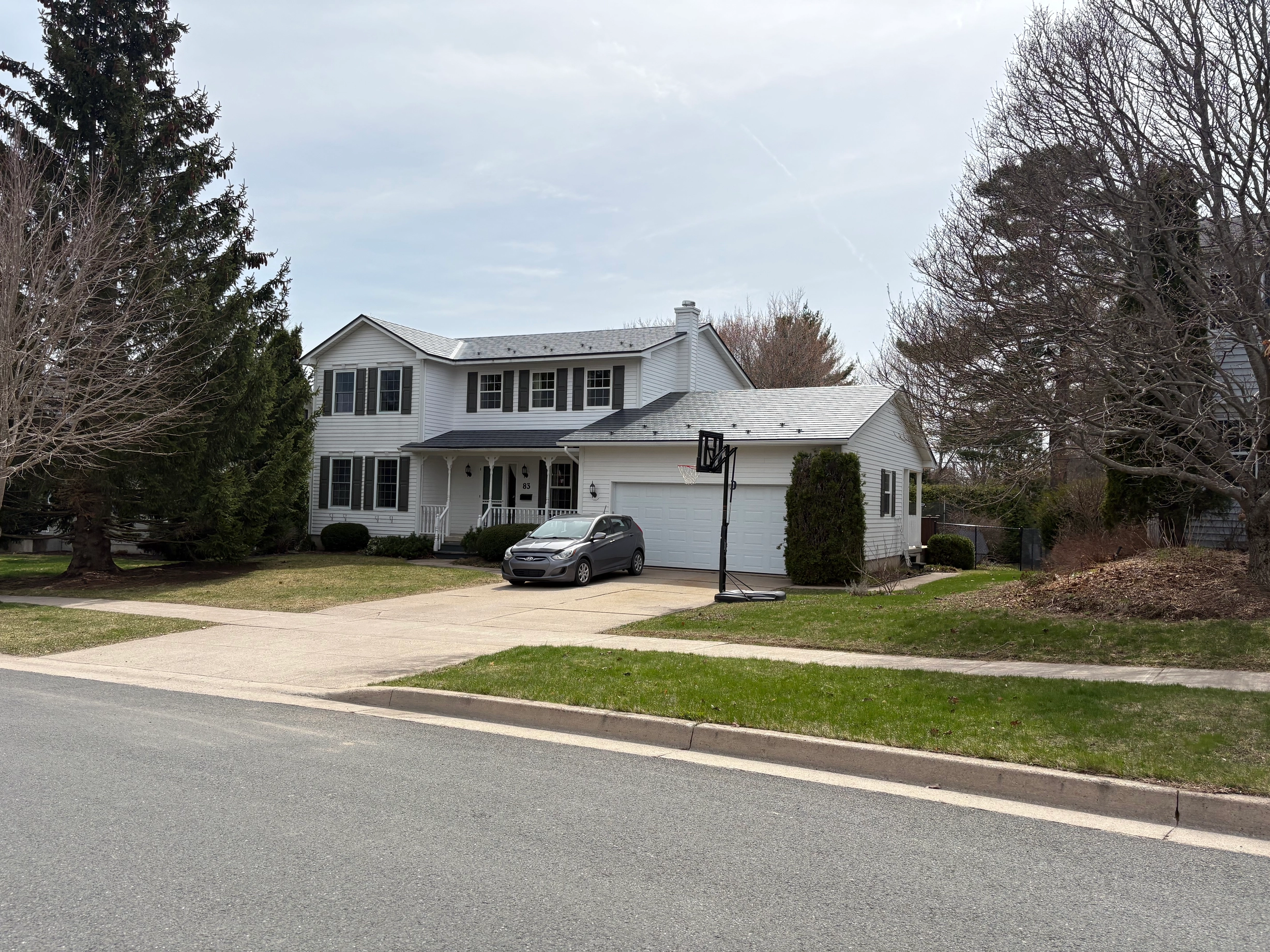 Deep Charcoal Interlock Slate aluminum roof on a white two-storey home with a metal roof among tall trees, Fredericton, New Brunswick
