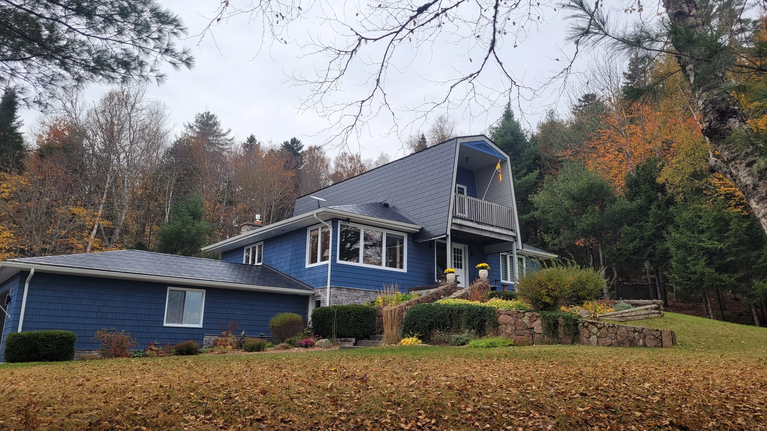 Black Interlock Slate aluminum roof on a blue one-storey cottage with dormers among tall pines, Utopia, New Brunswick