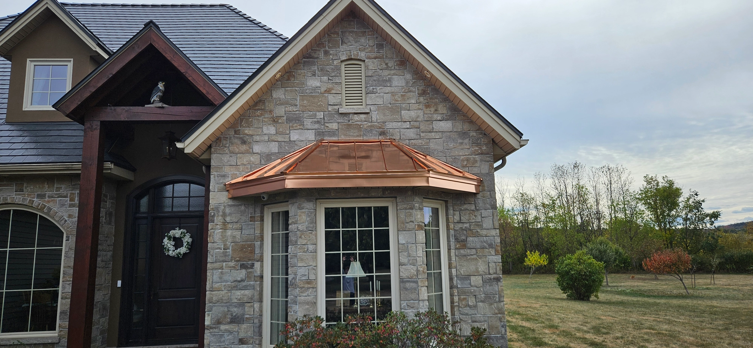 Deep Charcoal Interlock Slate aluminum roof on a two-storey home with a stone facade and a metal roof in a, Sussex, New Brunswick