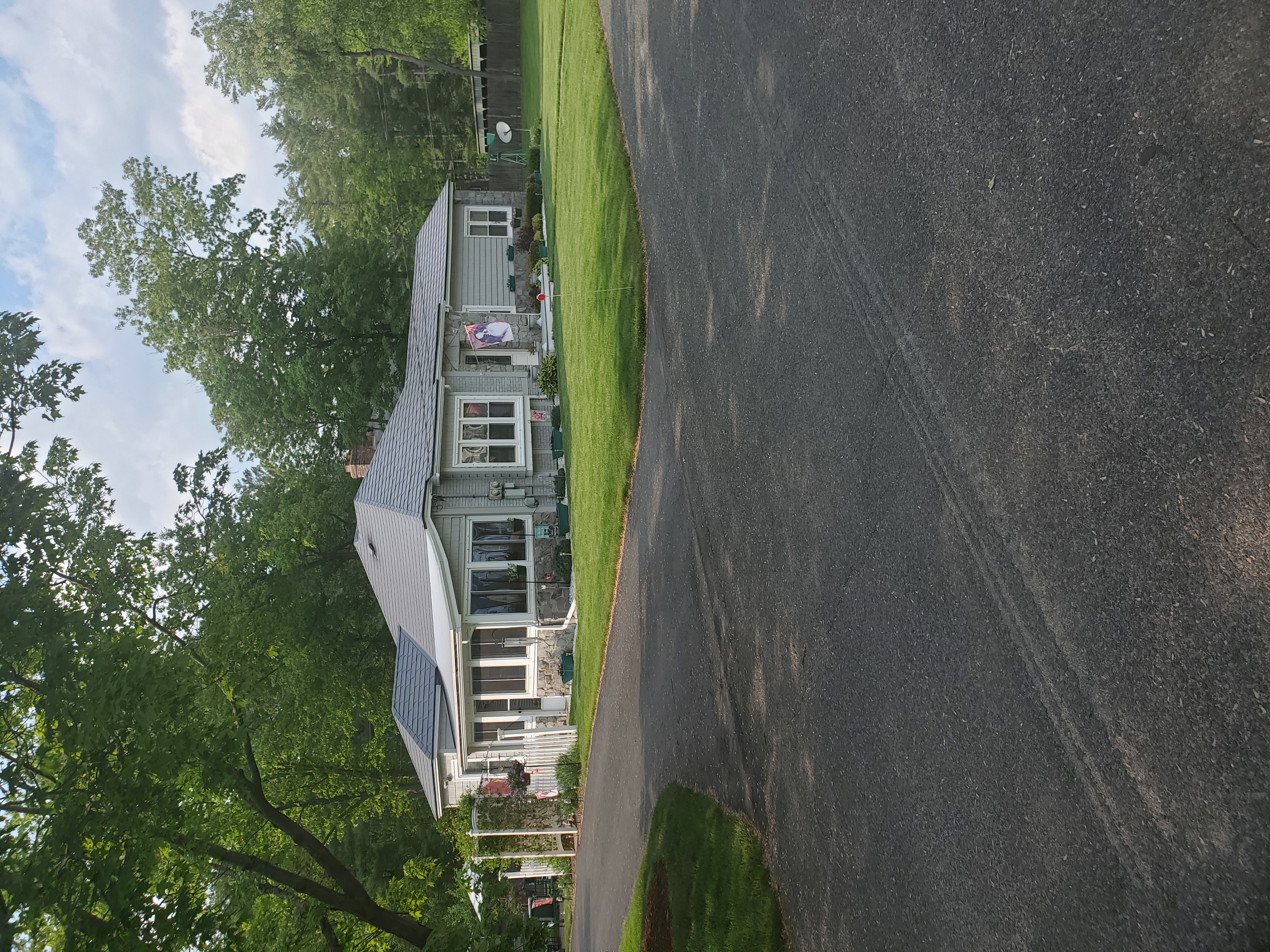 Charcoal grey Interlock aluminum slate metal roof on a single-story ranch home with hip roofline, stone facade, and screened porch, surrounded by mature trees in Keene, NH.