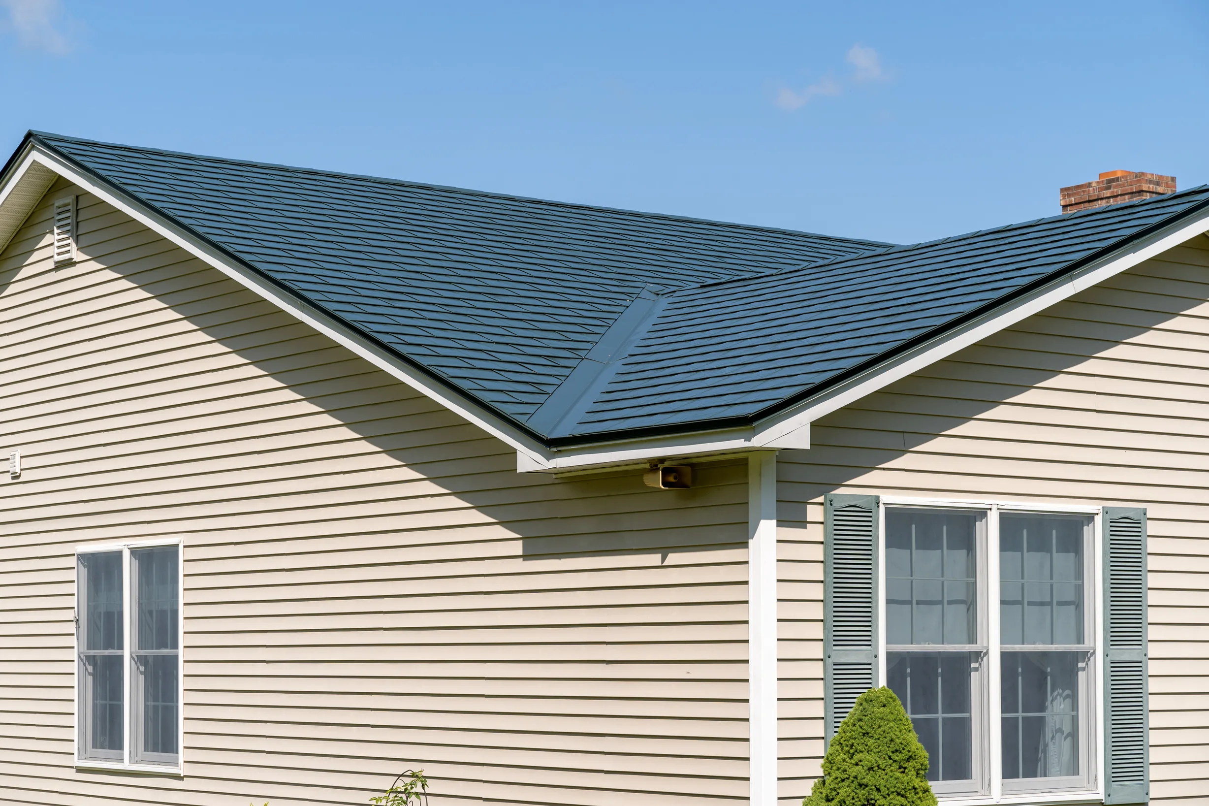 Hunter Green Interlock Slate aluminum roof on a beige one-storey home with a green metal roof among green, Sanbornville, New Hampshire