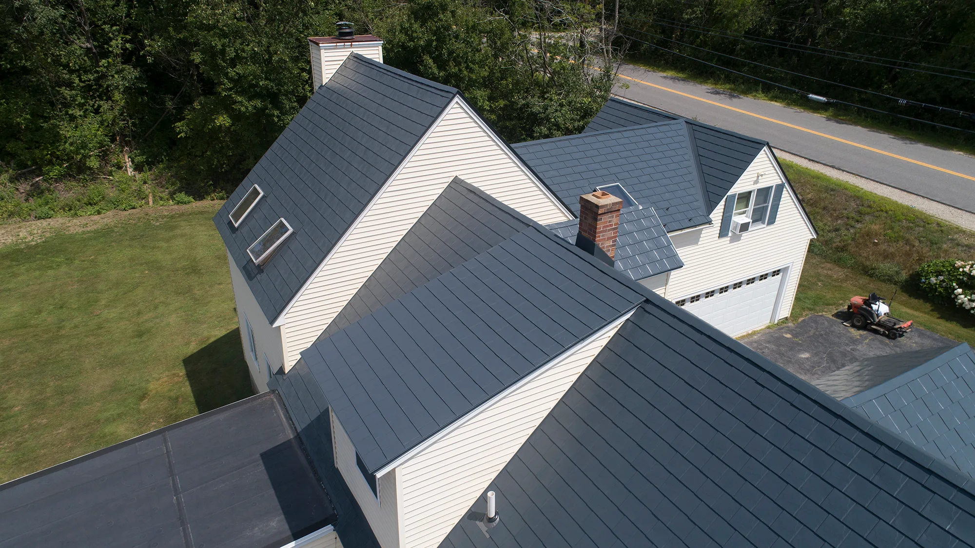 Deep Charcoal Interlock Slate aluminum roof on a white colonial home with dormers in a forested rural, Hooksett, New Hampshire