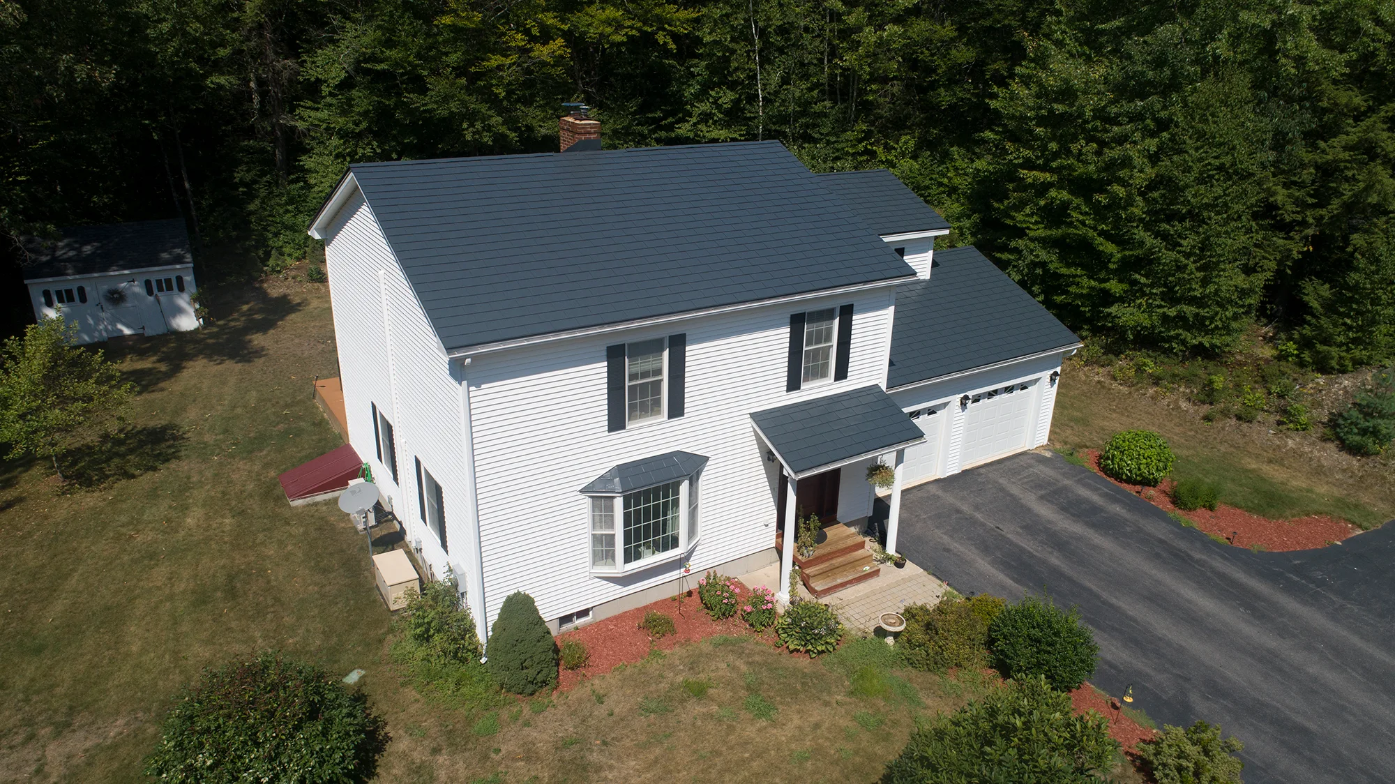 Charcoal Grey Interlock Slate aluminum roof on a white two-storey colonial home with dormers among tall, Webster, New Hampshire